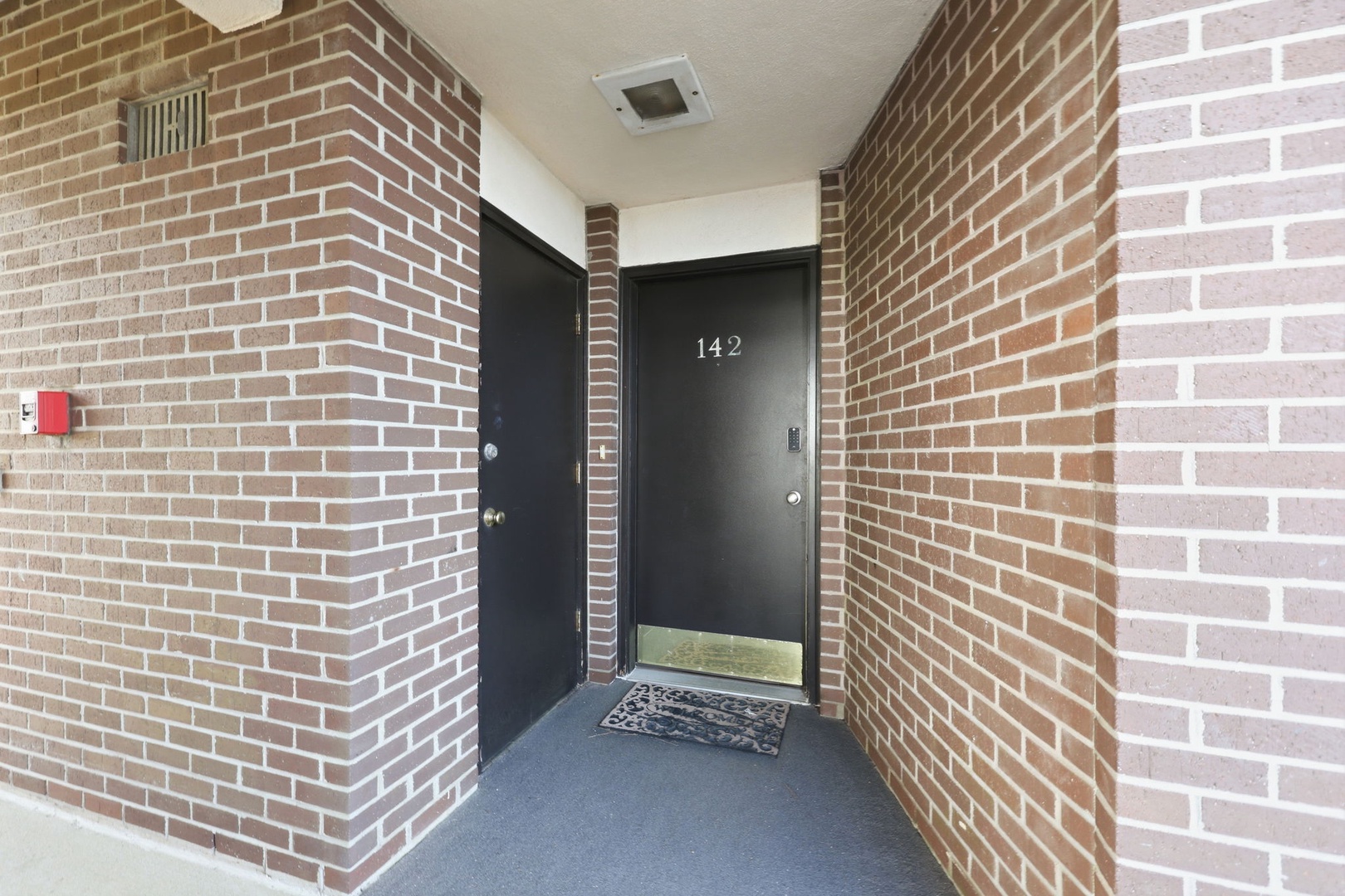 The private entrance to unit 142, framed by warm brick walls and a decorative welcome mat, marks the start of your stay.