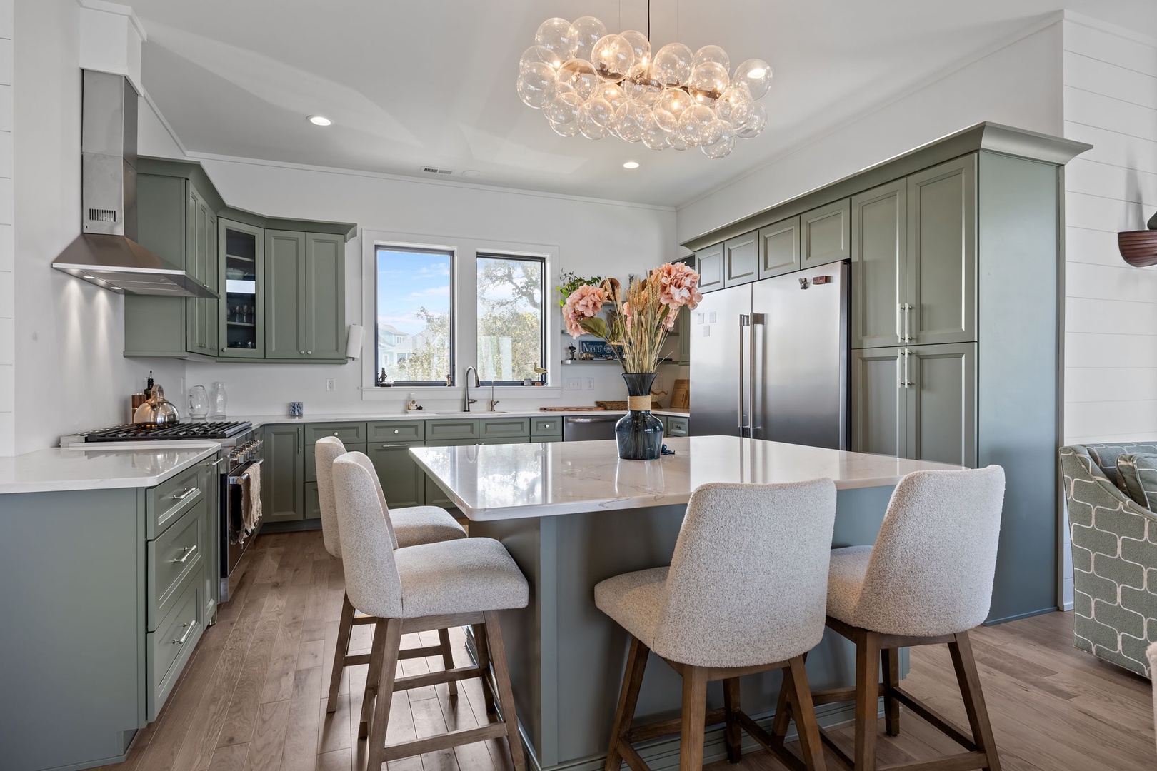 Your gourmet kitchen sparkles with sage cabinetry, gleaming counters, and a stunning chandelier overhead—perfect for culinary adventures.
