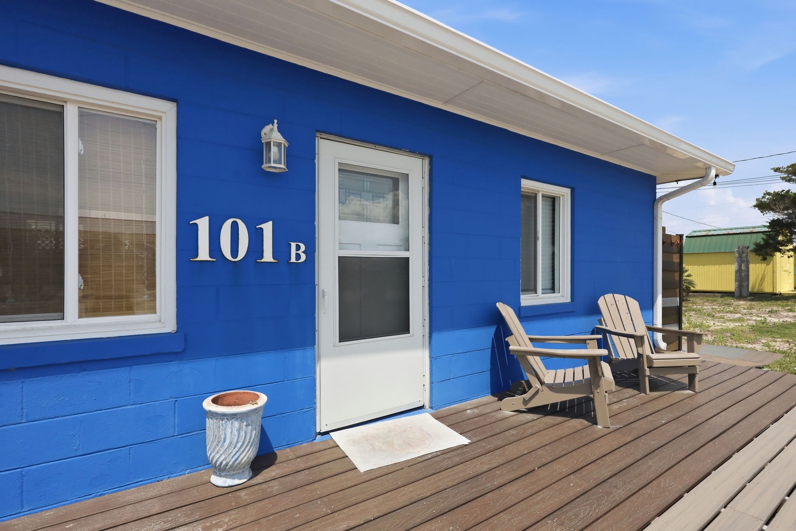 Unit 101B features a welcoming entrance with a spacious deck perfect for morning coffee or evening relaxation, marked by clear numbering and charming coastal touches.