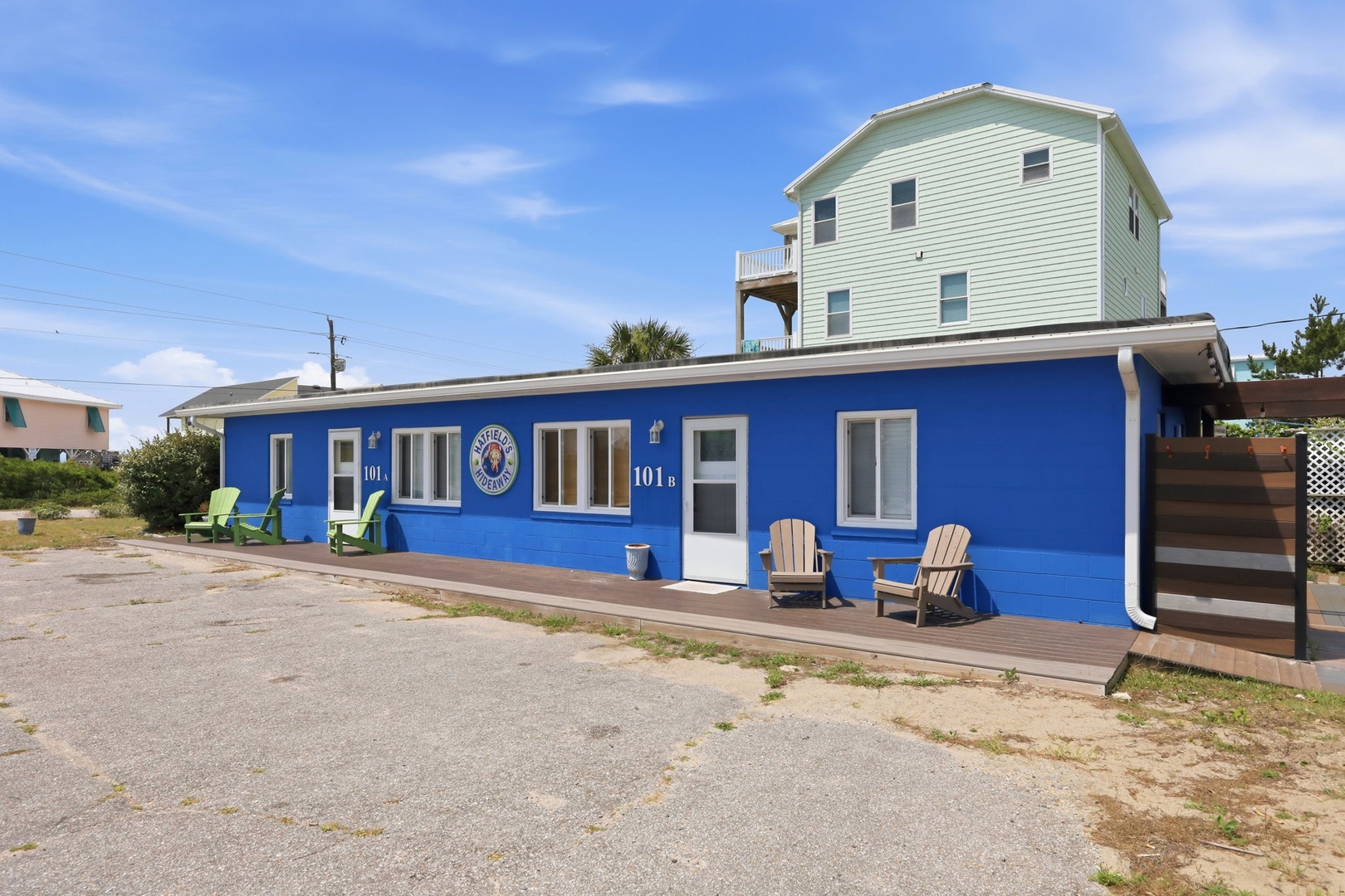 A vibrant blue beachside building with cozy Adirondack chairs on the wooden deck, offering easy access to the sand and surf.