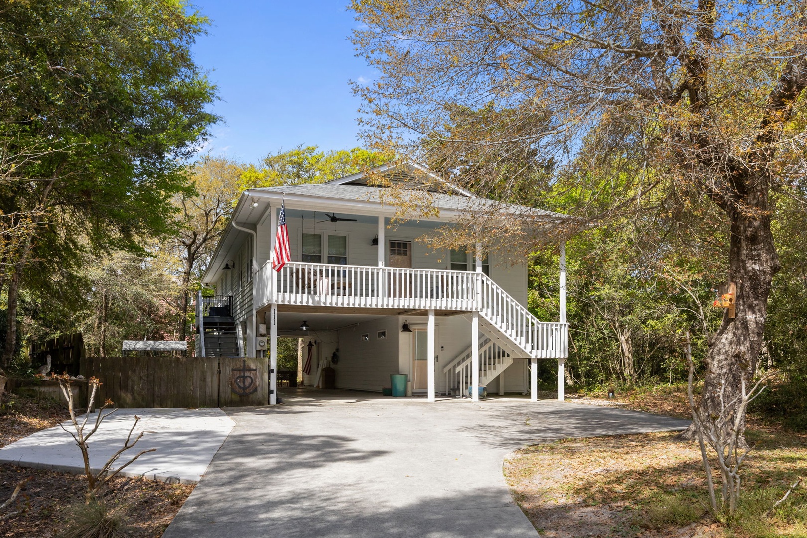 Charming elevated beach house with covered parking and spacious deck surrounded by mature trees.