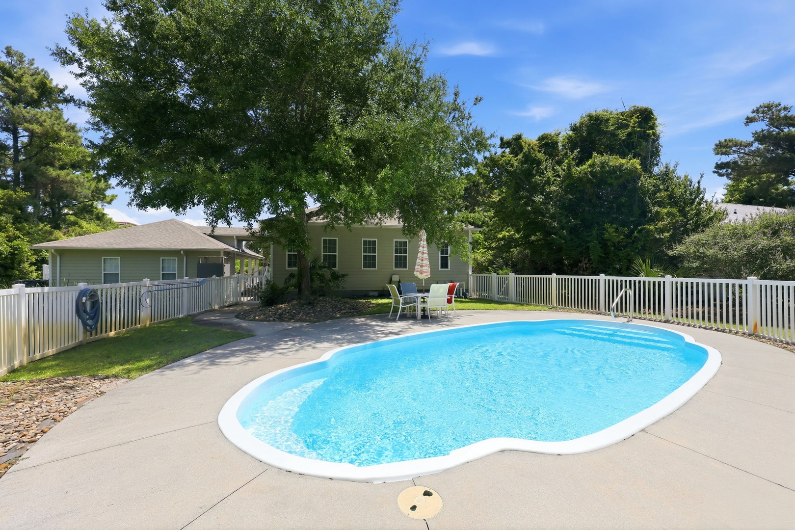 This inviting property features a private outdoor pool framed by a spacious, fenced-in backyard with mature trees and ample seating, creating a peaceful retreat for relaxing sunny days.