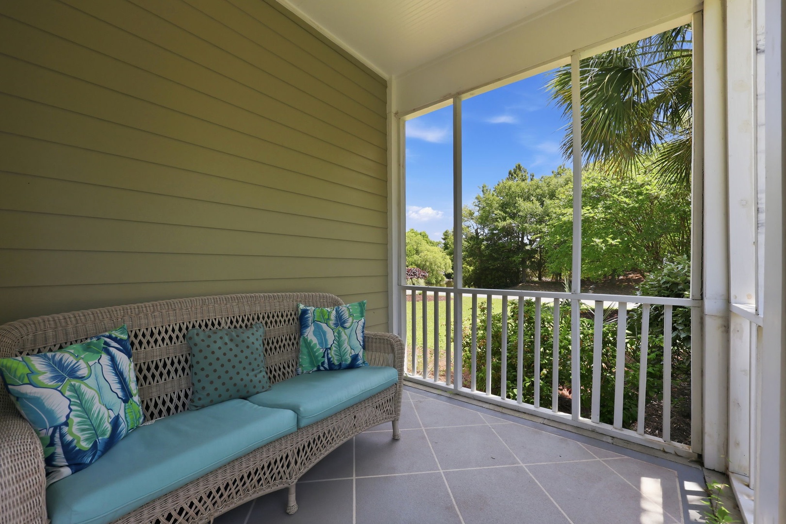 Relax on your private screened balcony with comfortable seating, where lush tropical greenery and brilliant blue skies create your peaceful retreat.