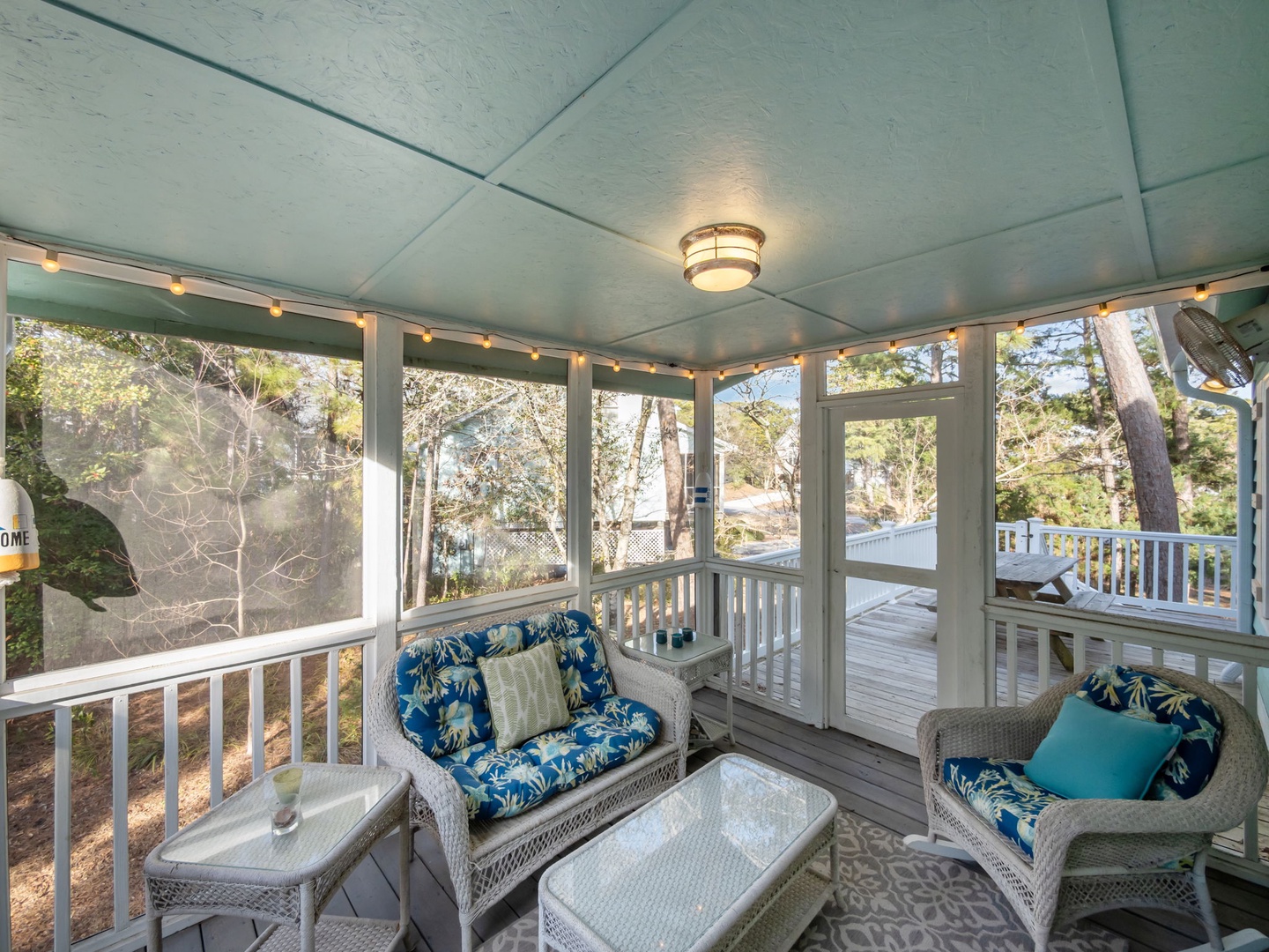 Relax in your screened-in porch with comfy wicker seating and string lights, overlooking peaceful wooded surroundings.