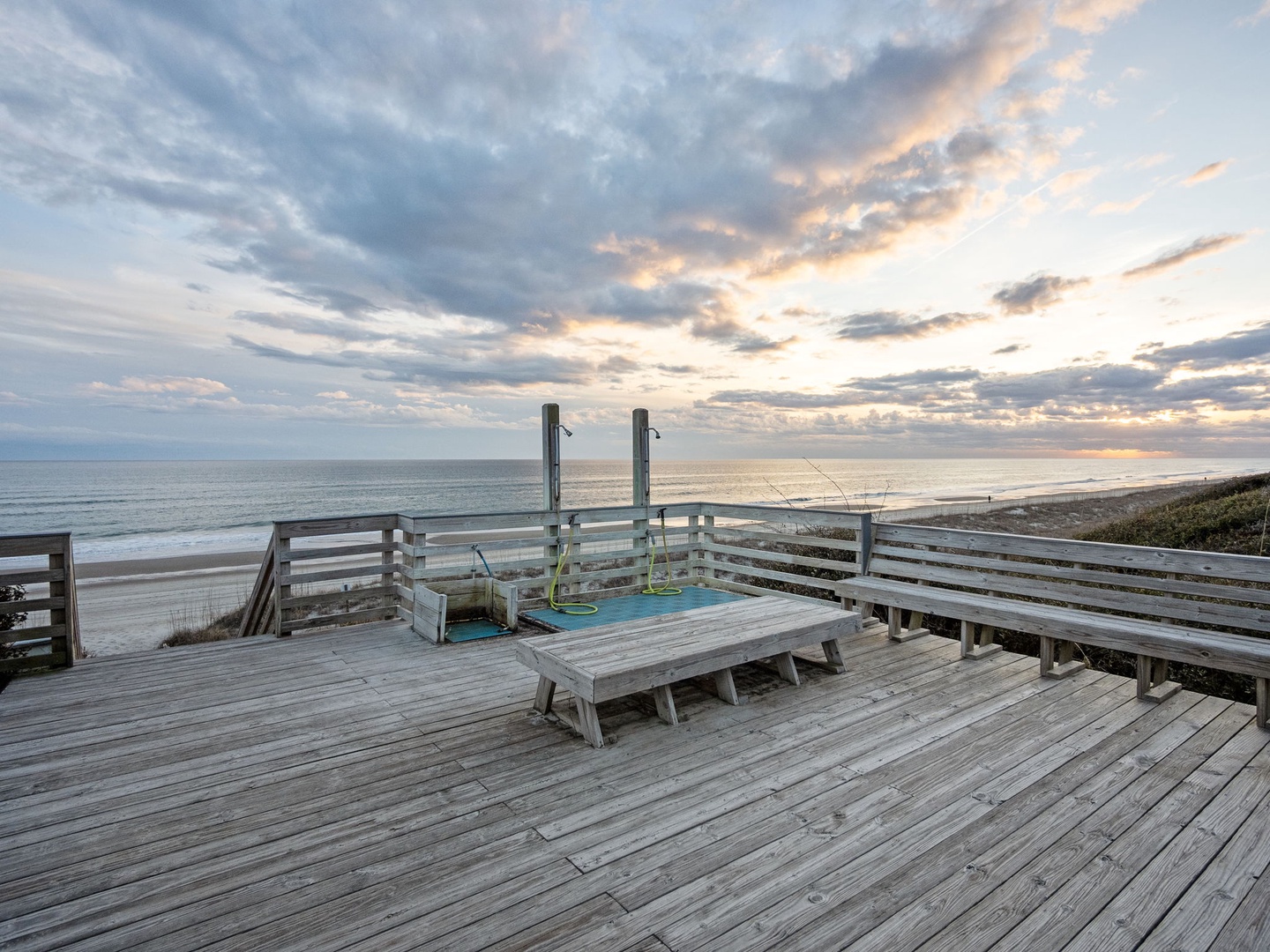 Wooden deck with seating overlooking ocean beach at sunset, perfect for evening relaxation.