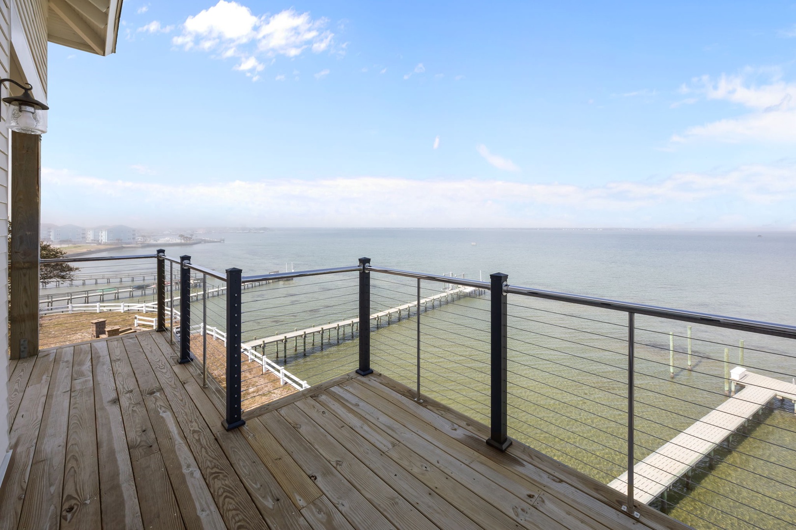 A stunning waterfront deck with panoramic ocean views and modern glass railings overlooking the peaceful coastline.