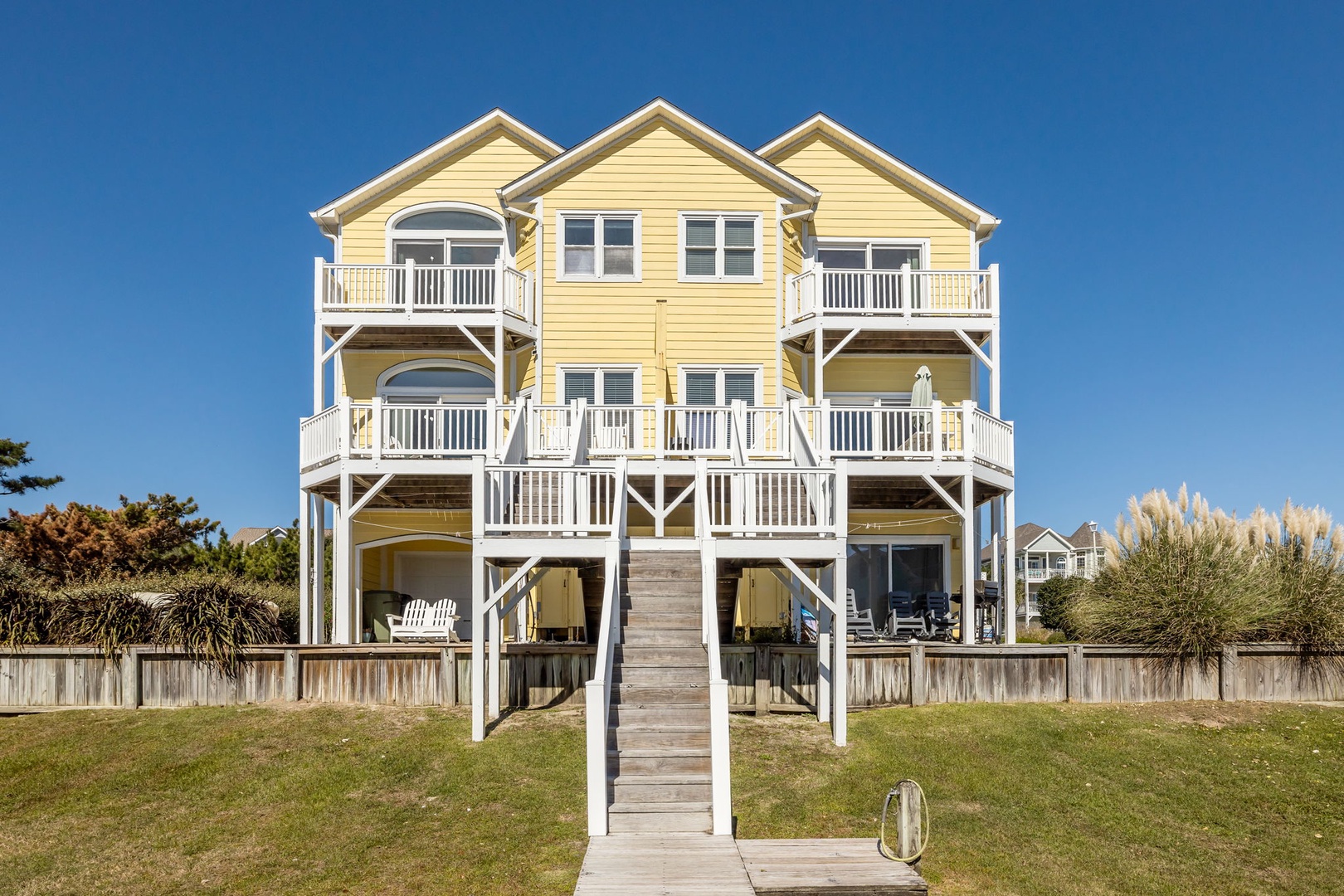 Charming beachfront property with yellow siding and multiple balconies, featuring elevated design and coastal architecture.