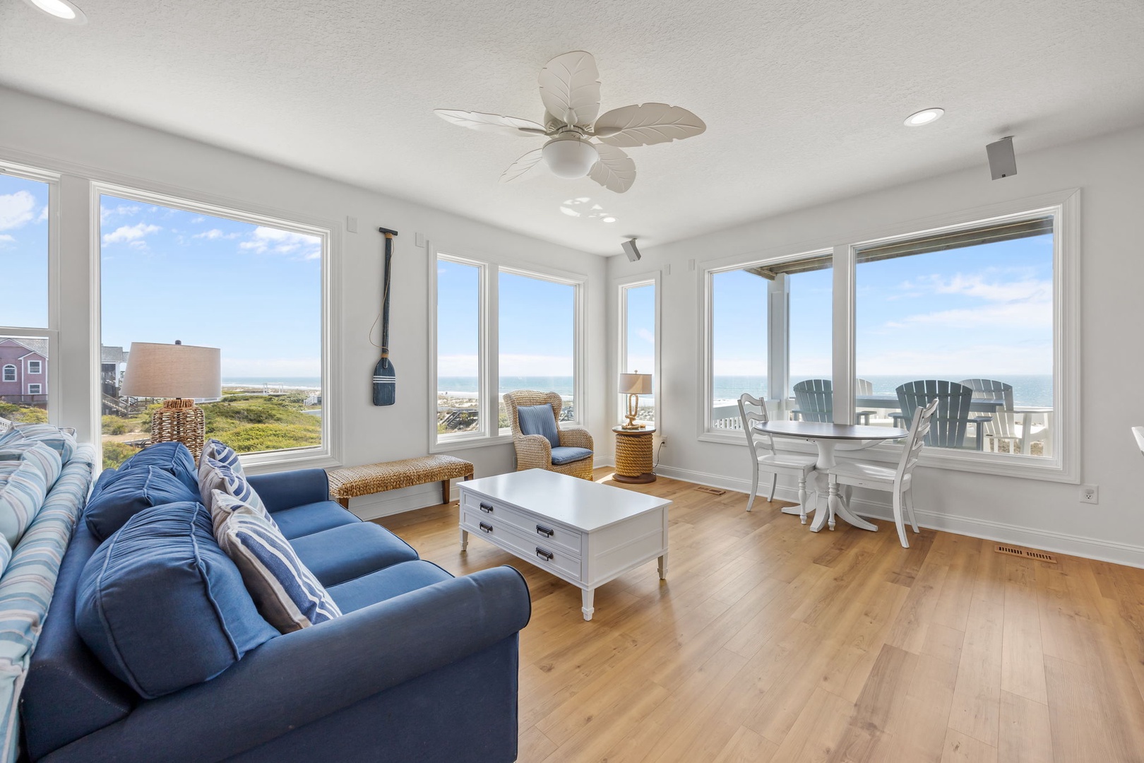 Unwind in your light-filled living space with panoramic ocean views through floor-to-ceiling windows and coastal breezes from the ceiling fan.