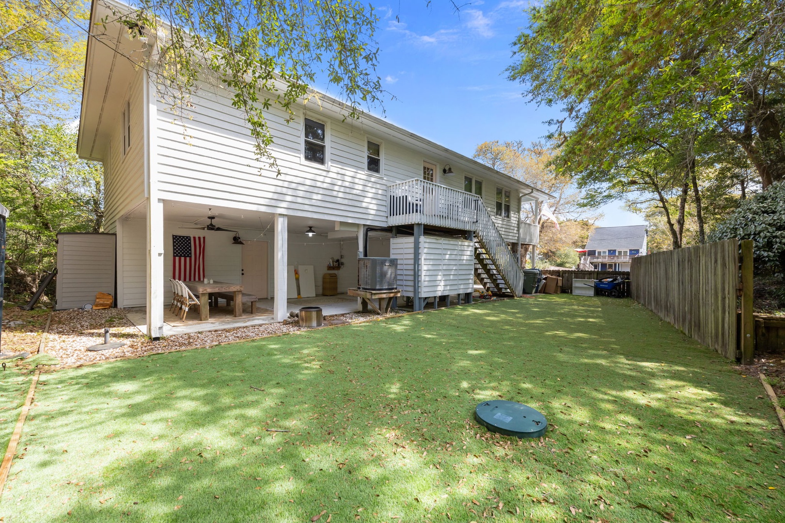 Two-story white property with covered outdoor area and spacious fenced backyard surrounded by mature trees.