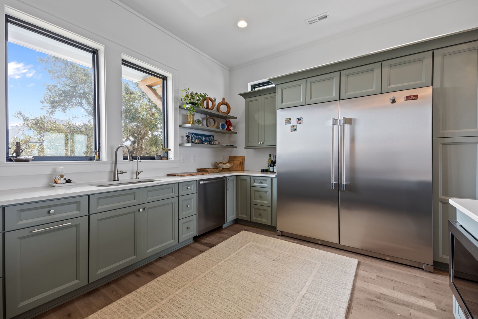 Cook with ease in your fully-equipped kitchen featuring sage-green cabinetry, stainless steel appliances, and garden views that inspire culinary creativity.