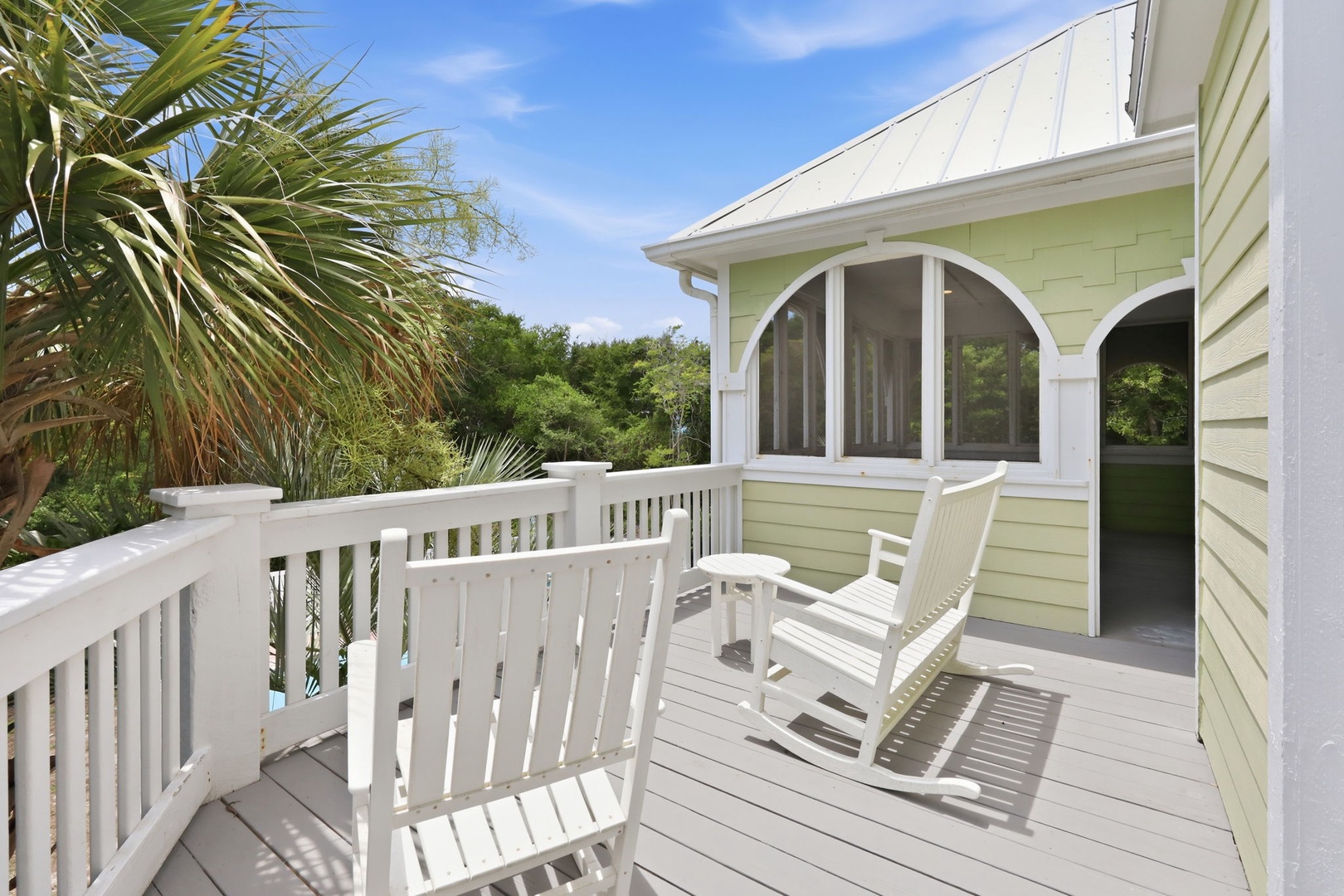 The property features a peaceful deck surrounded by lush tropical landscaping and clear blue skies, providing a serene arrival experience.
