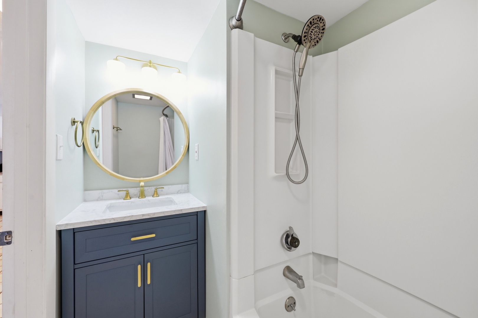 Your freshly updated bathroom features elegant gold accents, a sleek navy vanity with marble countertop, and a bright tub-shower combination ready for your comfort.