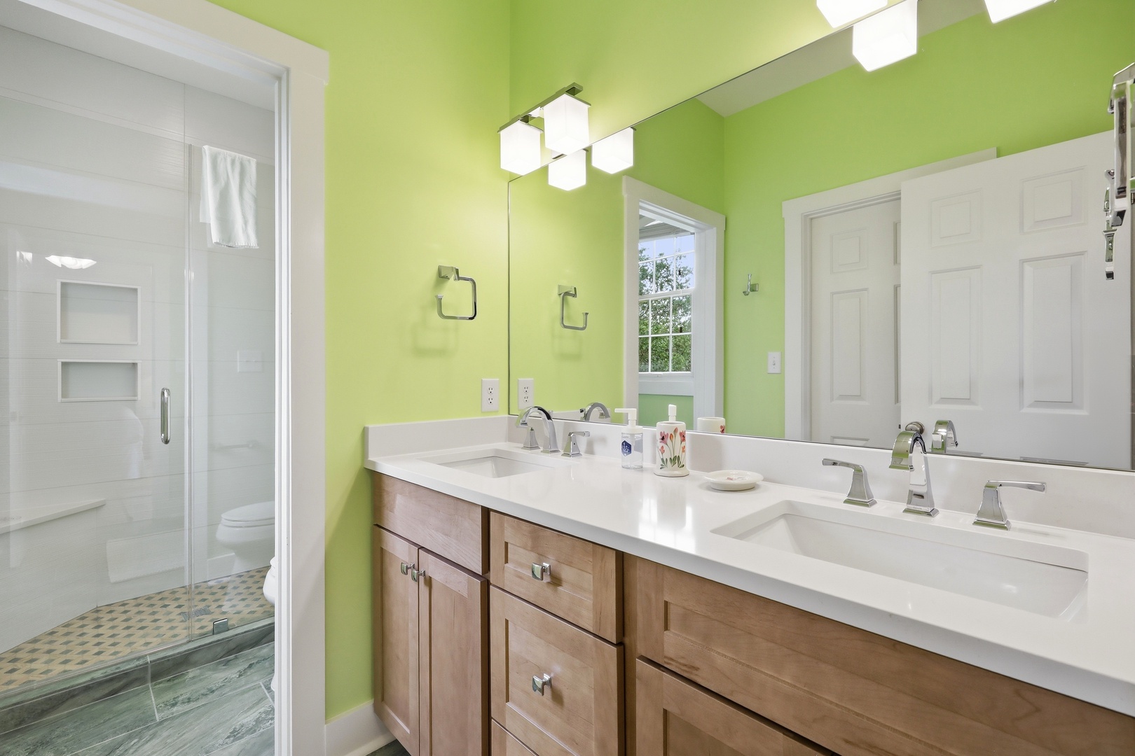 Your private bathroom features cheerful green walls, dual sinks with elegant fixtures, and a spacious walk-in shower with fresh white tile—perfect for refreshing mornings.