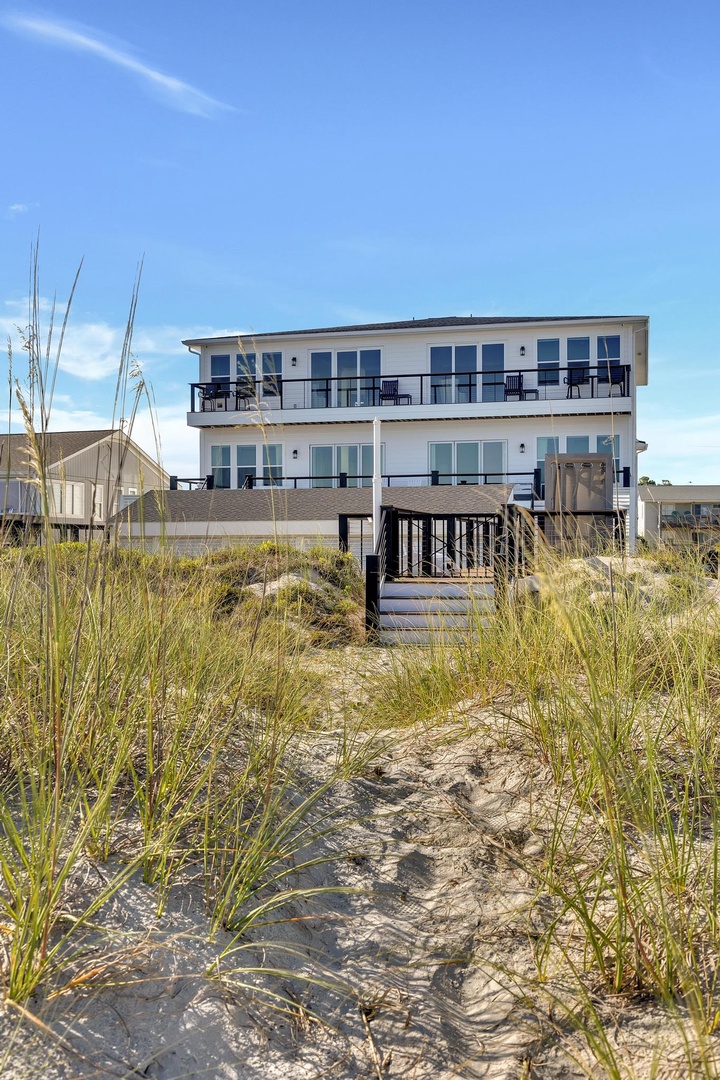 Modern beachfront property with sweeping balconies and direct access to the sandy shore, where blue skies meet coastal tranquility.
