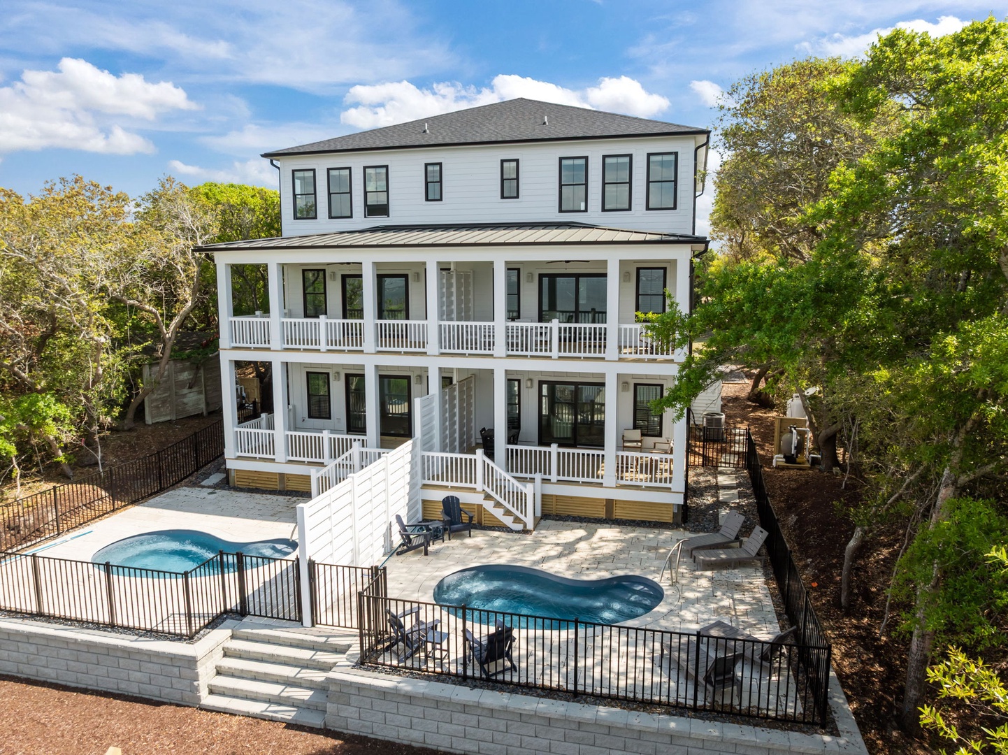 Modern three-story vacation home with wraparound porches, private pool, and hot tub nestled among lush trees.