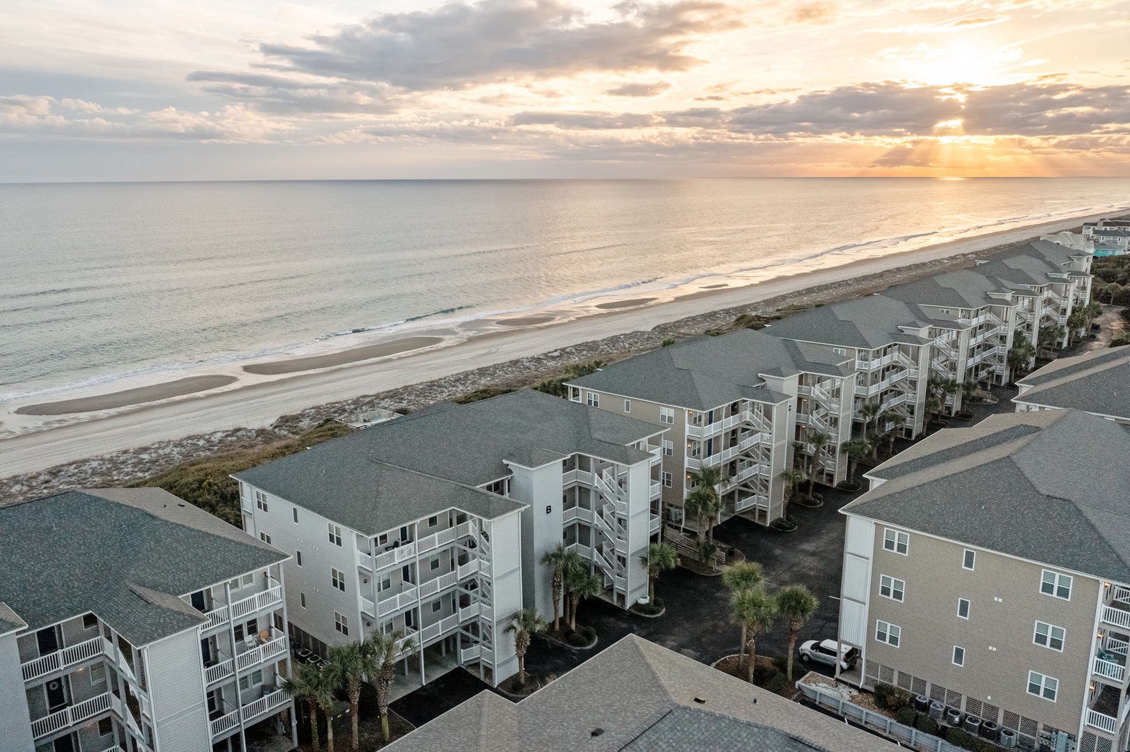 Beachfront resort buildings line pristine sandy shores under golden sunset skies, creating an idyllic coastal retreat setting.