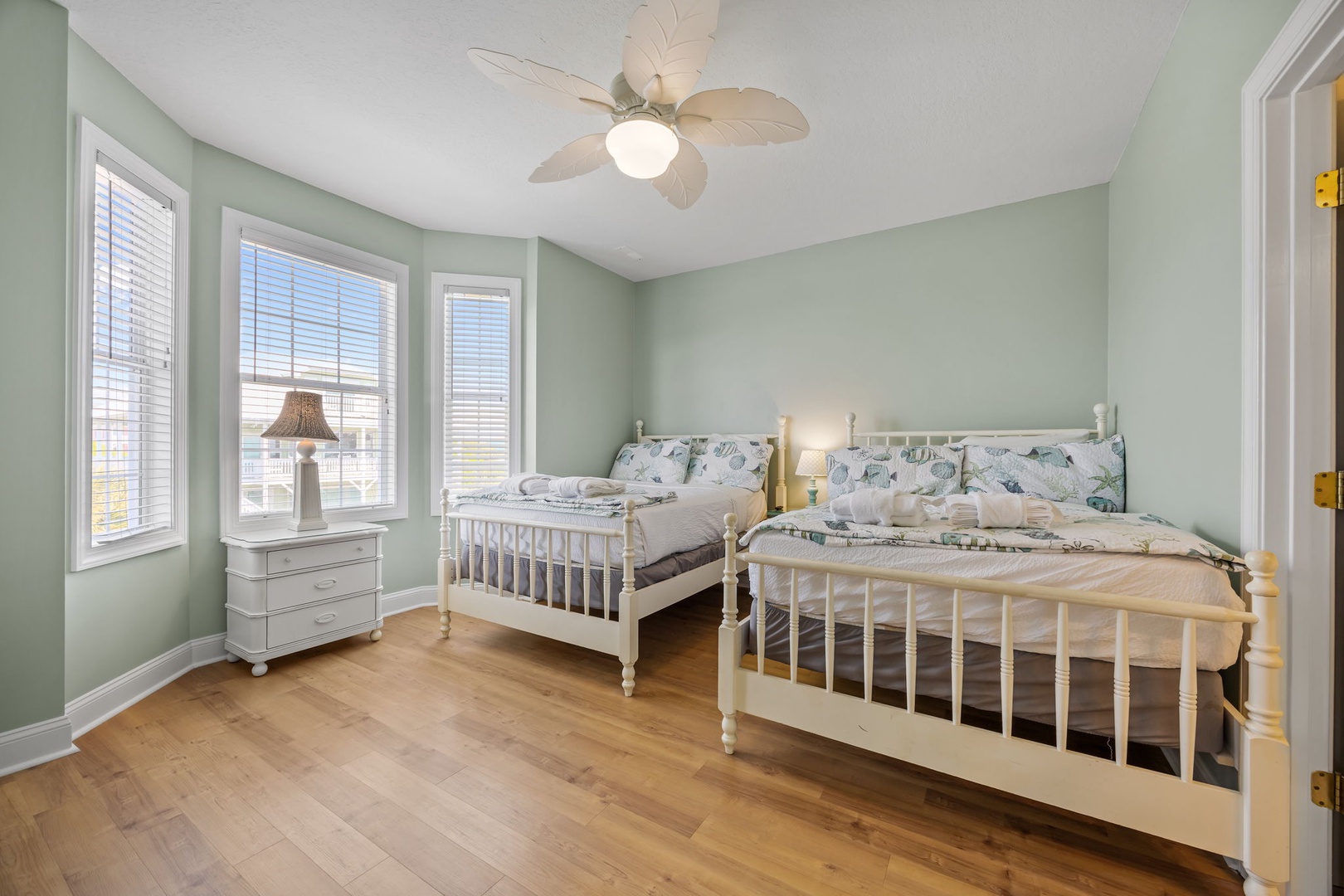 Unwind in your serene retreat featuring twin beds with botanical linens, calming sage walls, and a gentle ceiling fan.