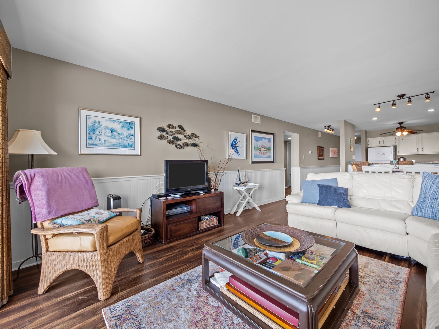 Relax in your spacious living room with coastal art, comfortable seating, and an open kitchen perfect for beach vacation evenings.