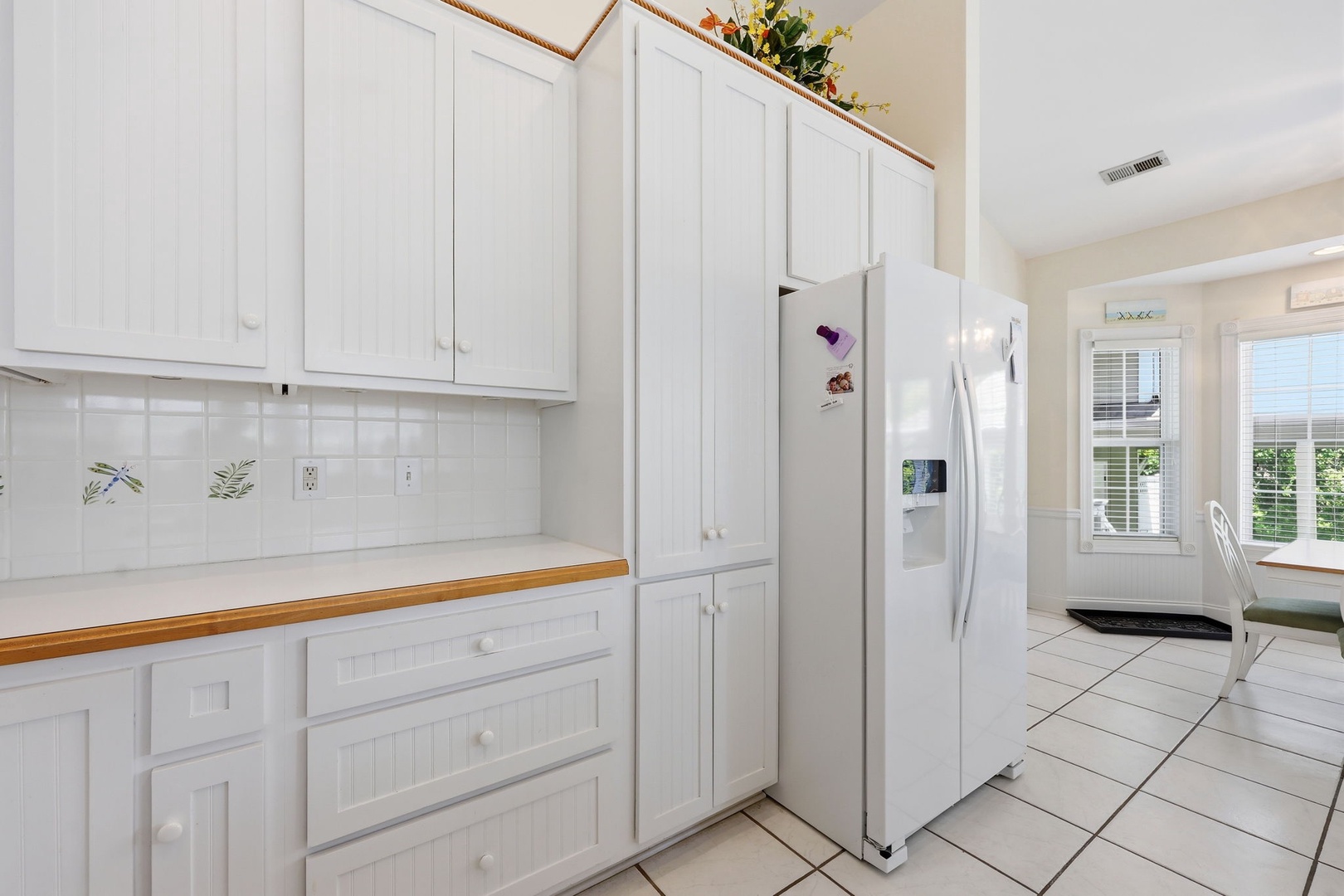 This bright, airy kitchen features classic white cabinetry, clean tile counters, and modern appliances ready for your culinary adventures. Natural light streams through windows overlooking peaceful greenery outside.