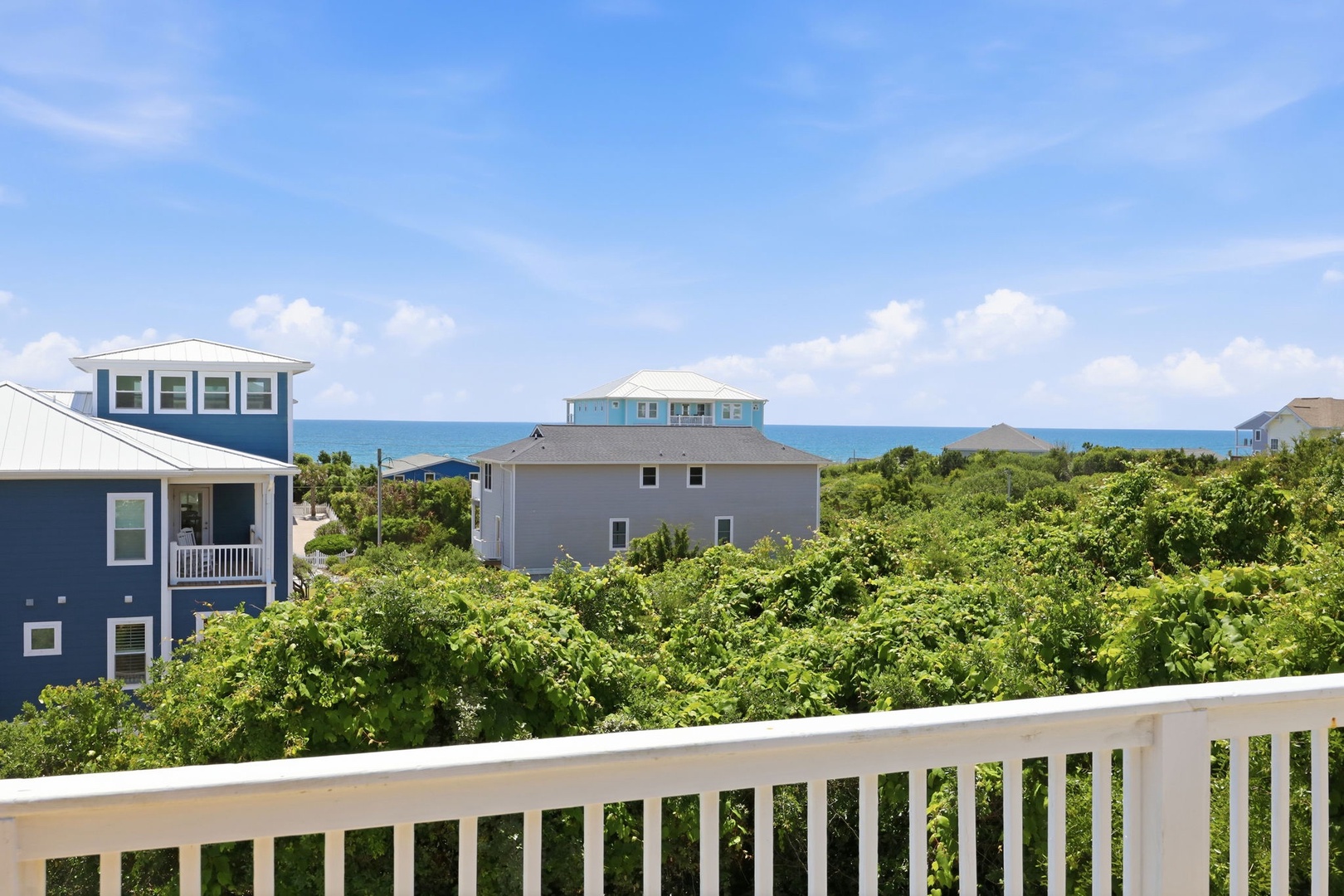 Coastal homes nestle amid lush greenery, with the sparkling ocean visible beyond the dunes, marking your arrival to this beach community.