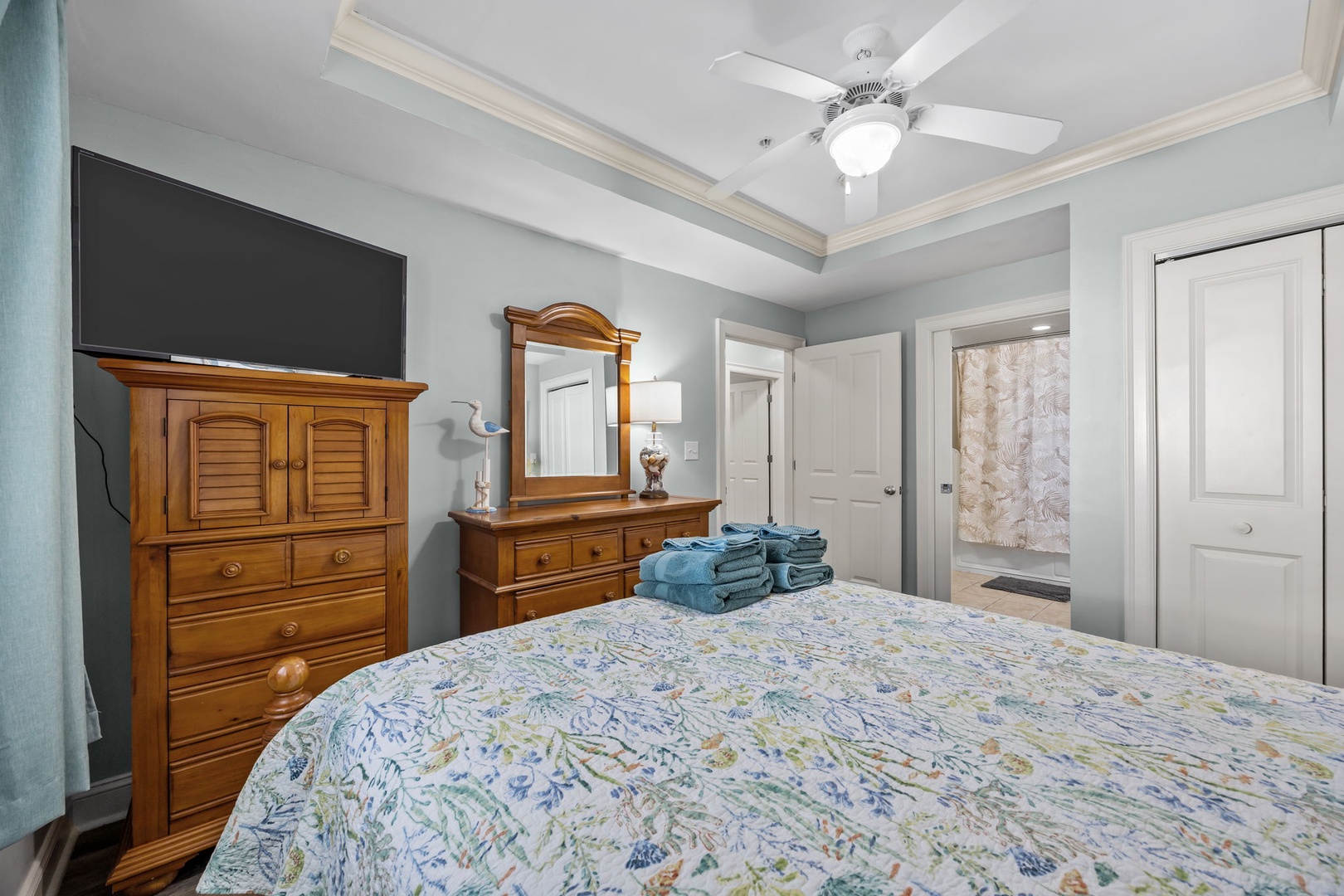 Your restful bedroom features elegant wooden furniture, a wall-mounted TV, and fresh towels waiting for your arrival.