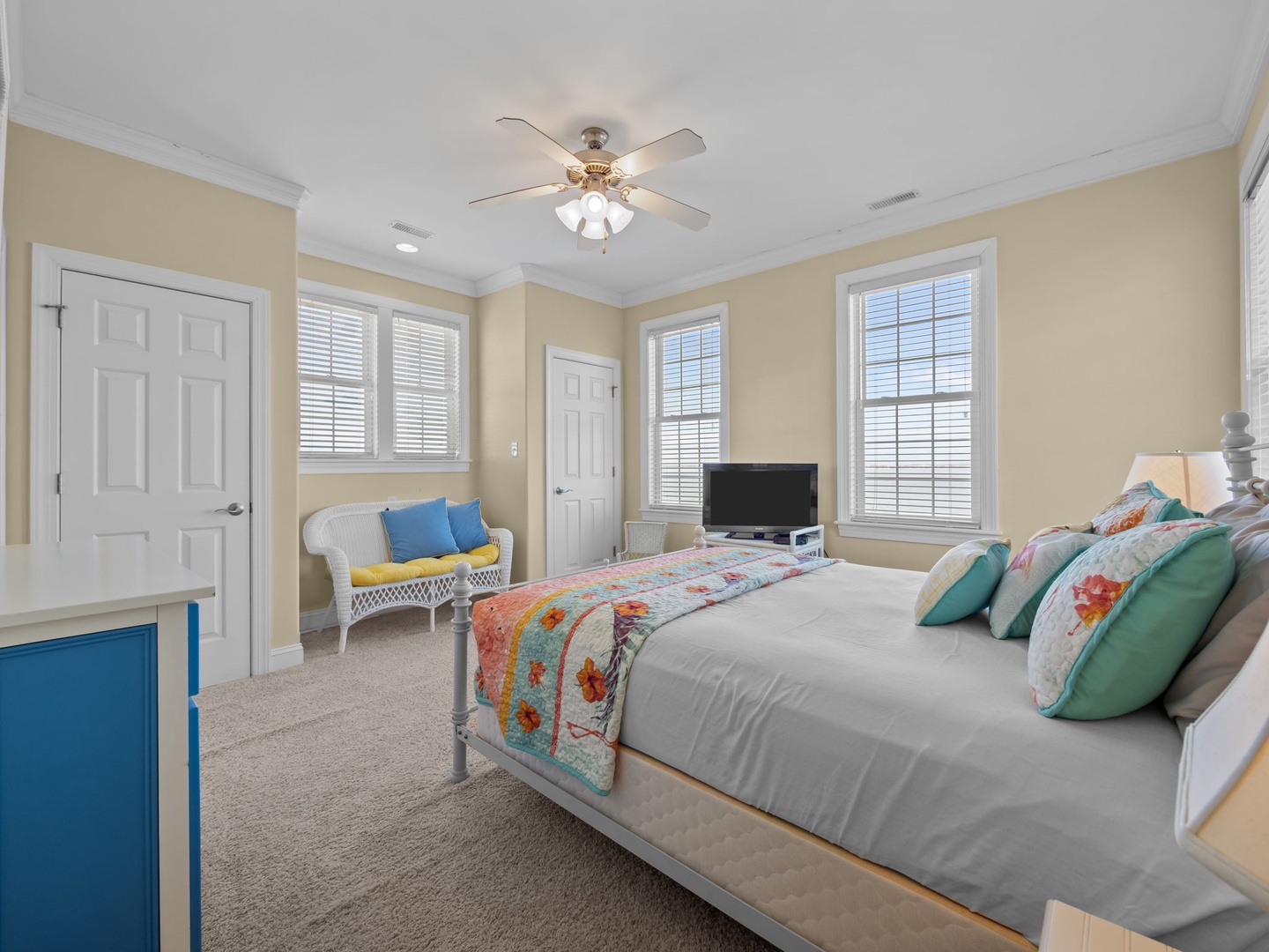 Unwind in your bright, cheerful bedroom with colorful quilted bedding, cozy seating nook, and natural light streaming through multiple windows.