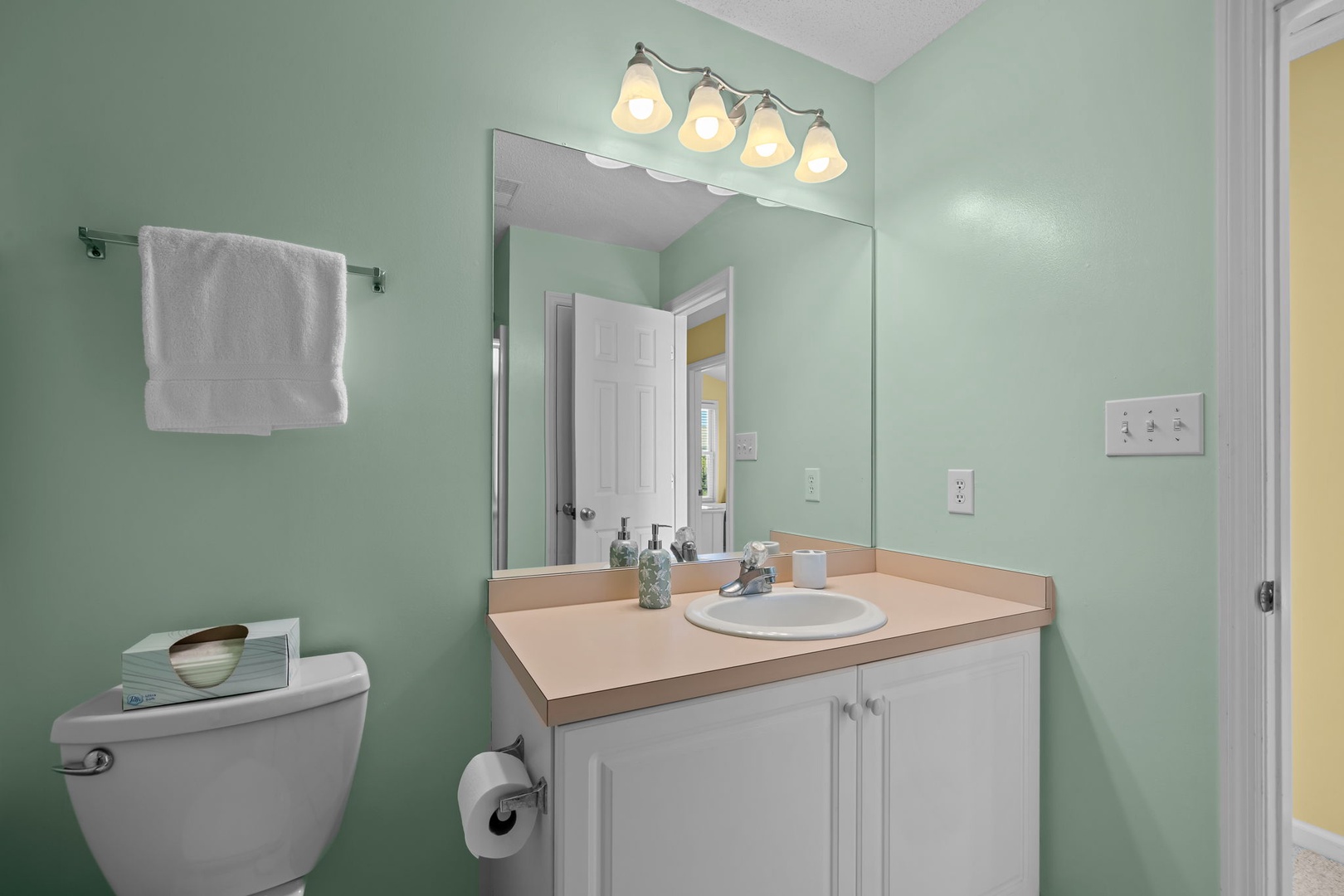 Refresh in your private bathroom with soothing mint walls, warm vanity lighting, and fresh towels ready for your stay.