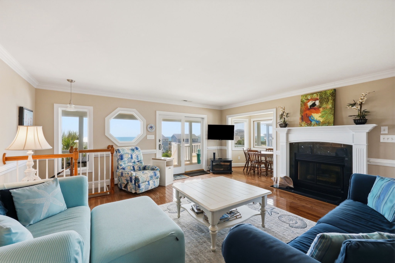 Relax in your bright, coastal living room with a crackling fireplace, sweeping ocean views through multiple windows, and plush seating perfect for unwinding after a day at the beach.