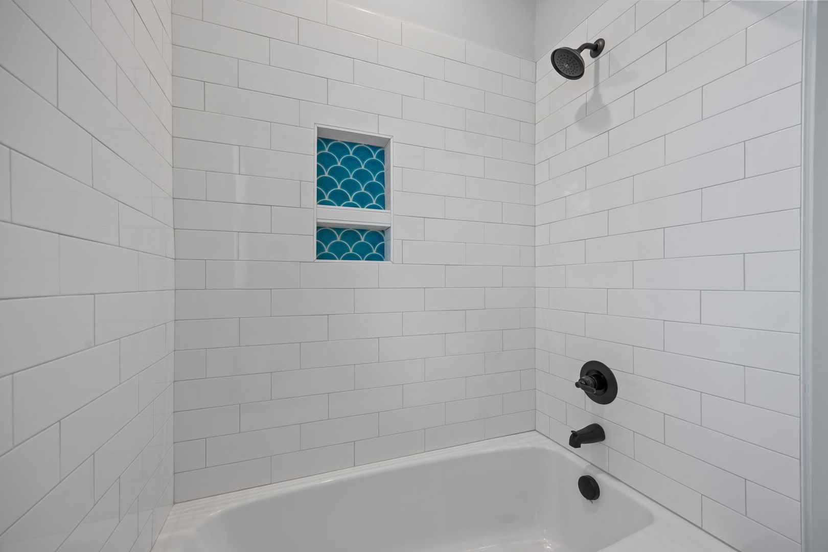 Unwind in your pristine spa-like bathroom featuring clean subway tiles, a spacious tub, and charming turquoise accent niches for a refreshing retreat.