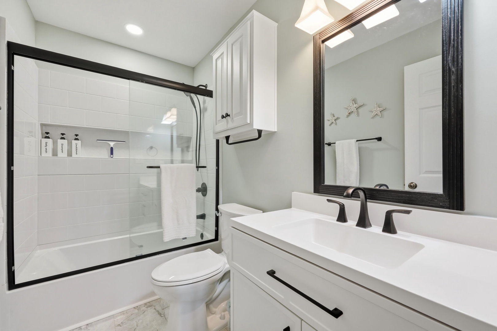 Refresh in your pristine bathroom featuring a sleek walk-in shower, coastal starfish accents, and modern fixtures—your personal spa awaits after beach adventures.