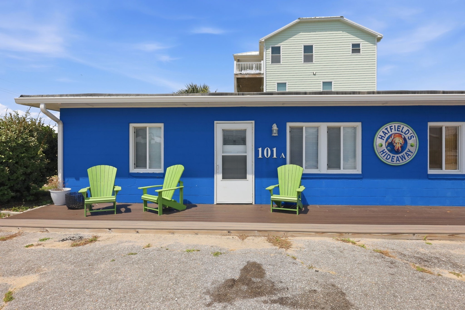 Charming blue beachside property with bright green seating on the deck welcomes guests to their coastal retreat at 101A Bluefields Hideaway.