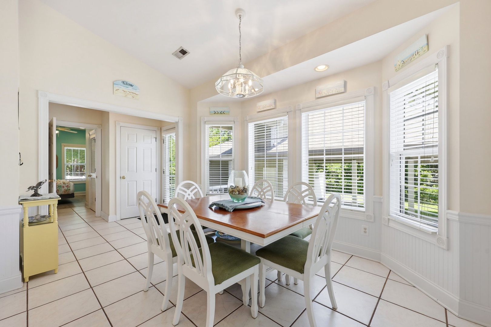 Gather around this bright dining space for meals bathed in natural light. The coastal-inspired table seats eight comfortably, with white cabinetry and tile flooring creating a fresh, airy feel.