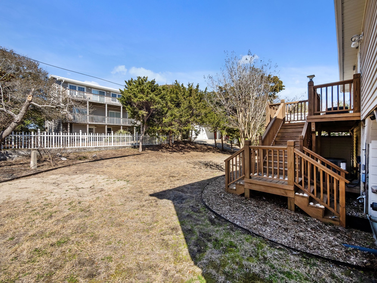 Wooden deck and stairs lead to a spacious backyard surrounded by coastal trees and neighboring properties.