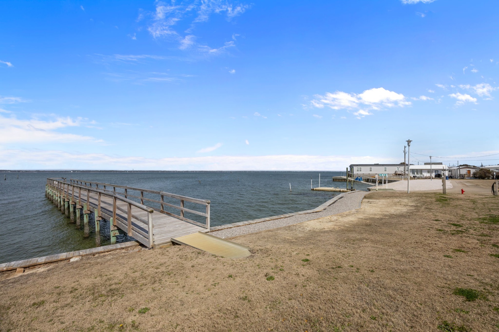 Peaceful waterfront location with wooden pier extending into calm waters, surrounded by coastal community buildings.