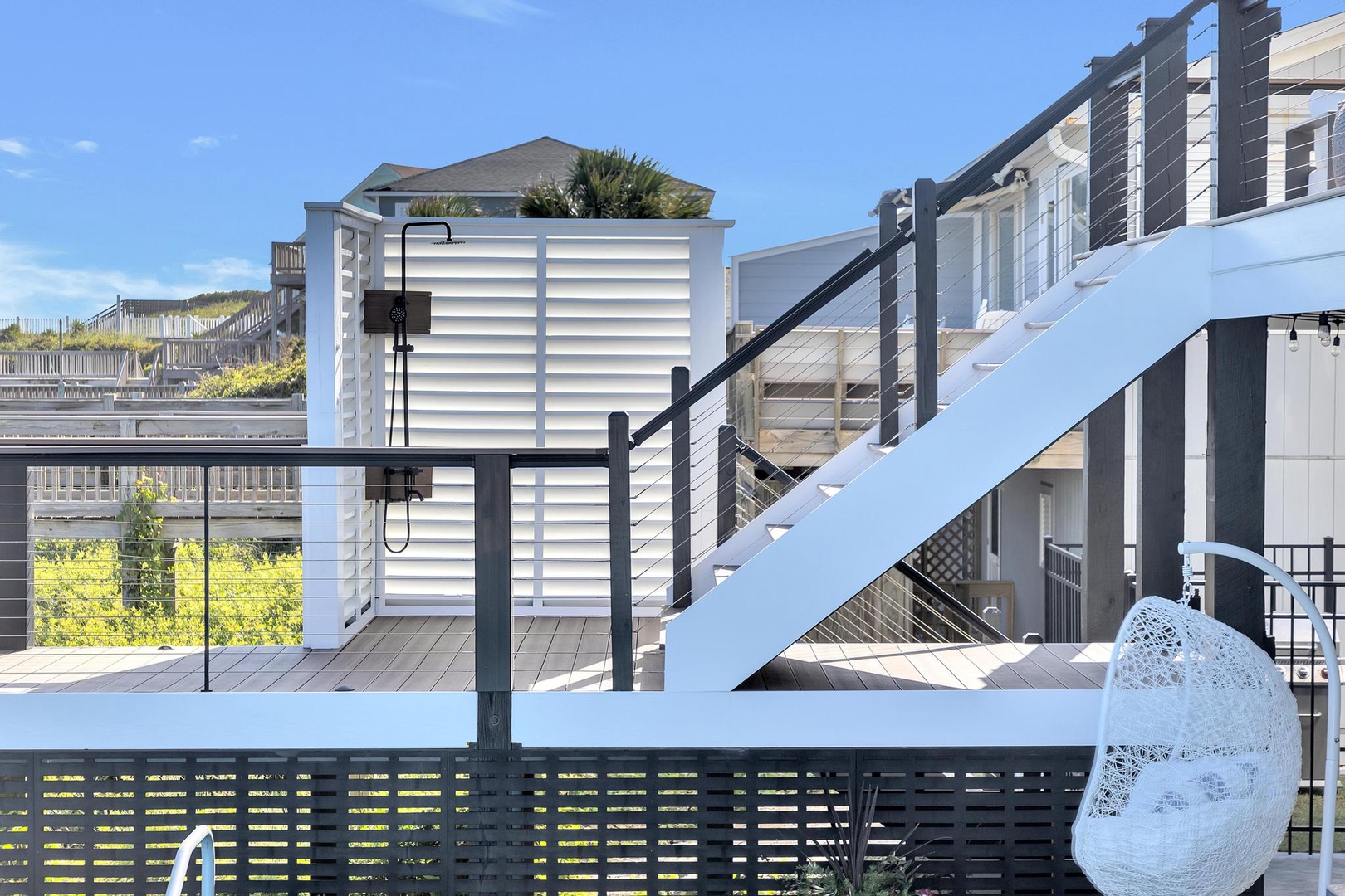 This coastal property features multiple tiered decks and staircases, offering easy access to beach activities. The modern exterior is surrounded by dunes and neighboring homes.