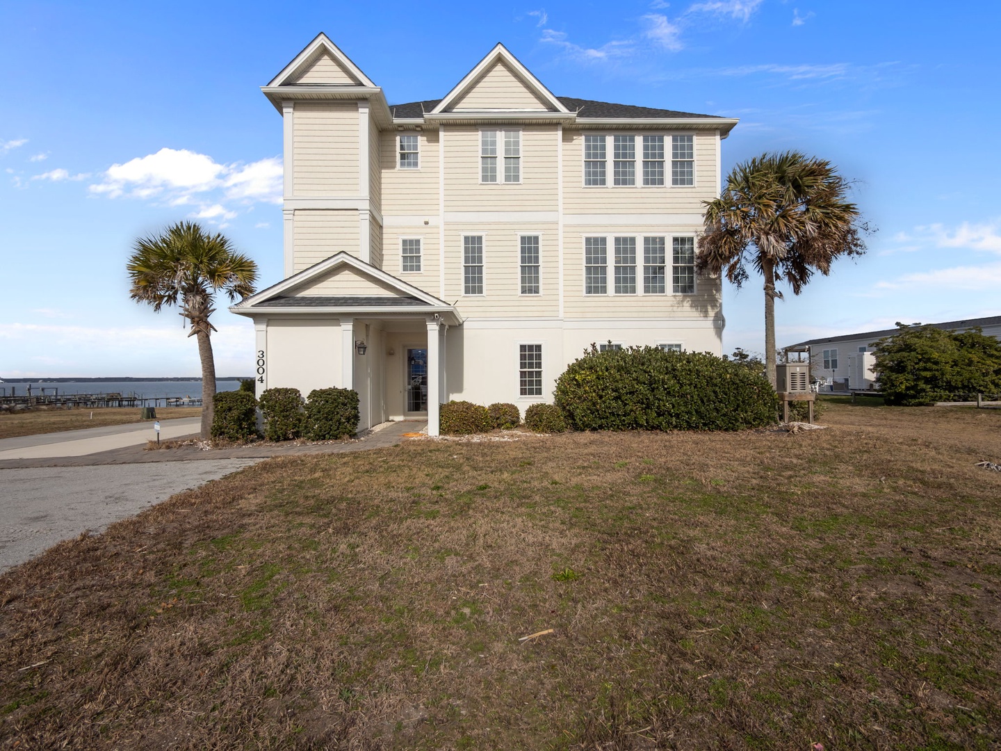 A beautiful three-story waterfront vacation home featuring classic coastal architecture with palm trees and nearby water access.