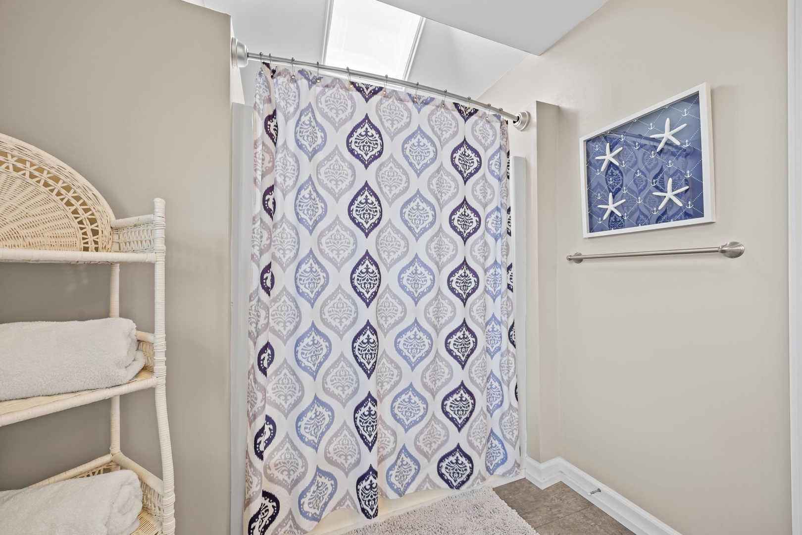 Fresh towels await you in this bright bathroom featuring a stylish patterned shower curtain and coastal-themed artwork.