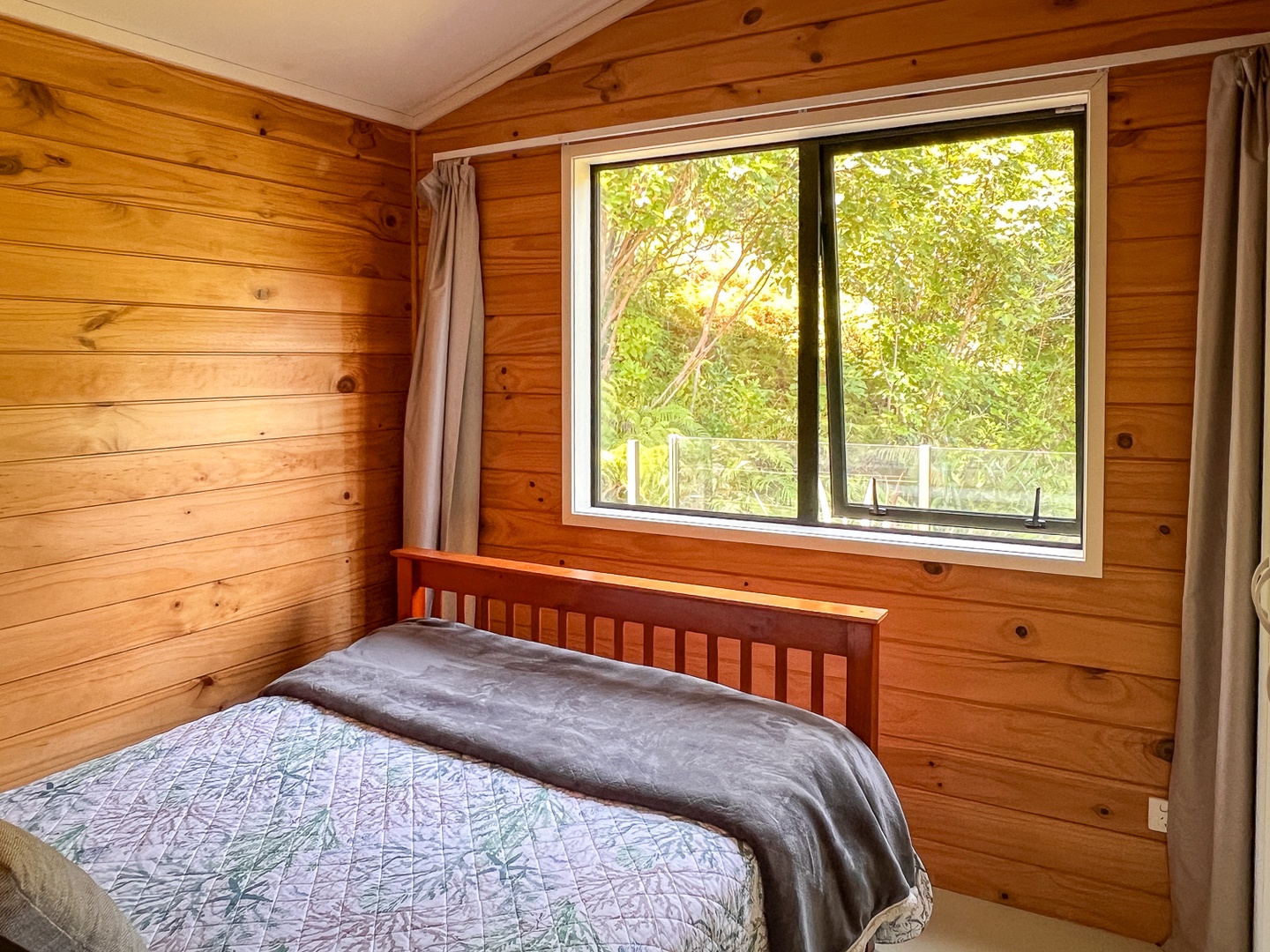 Wake up surrounded by warm pine walls in your cozy bedroom, where natural light streams through your window overlooking lush greenery.