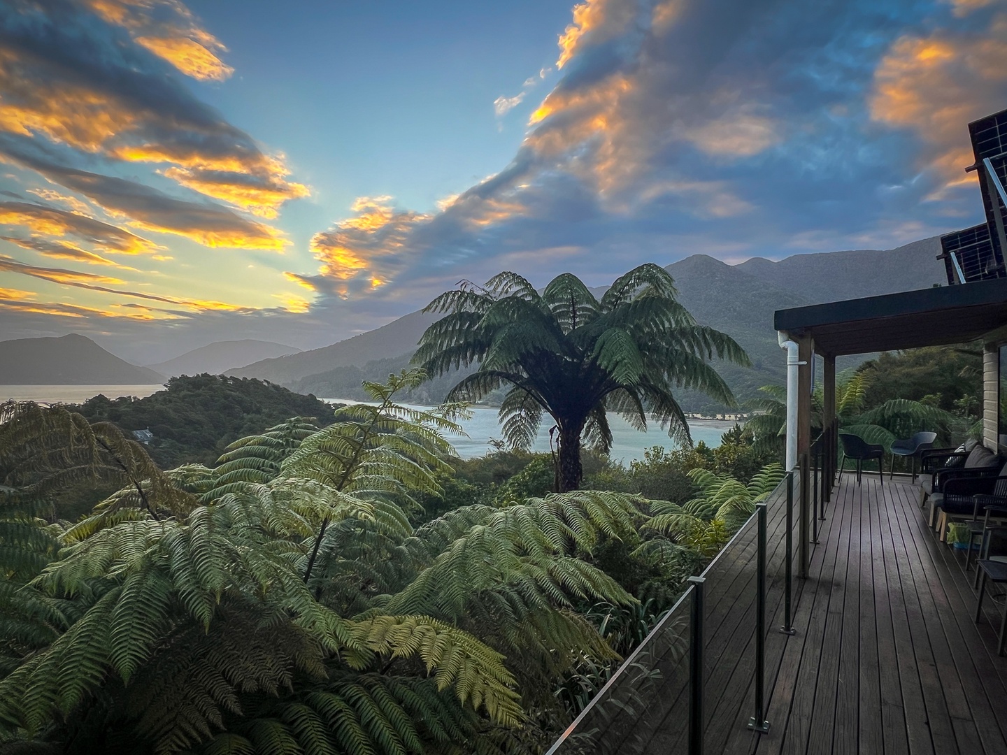 Spectacular mountain and lake views frame this elevated deck overlooking native fern forests at sunset.