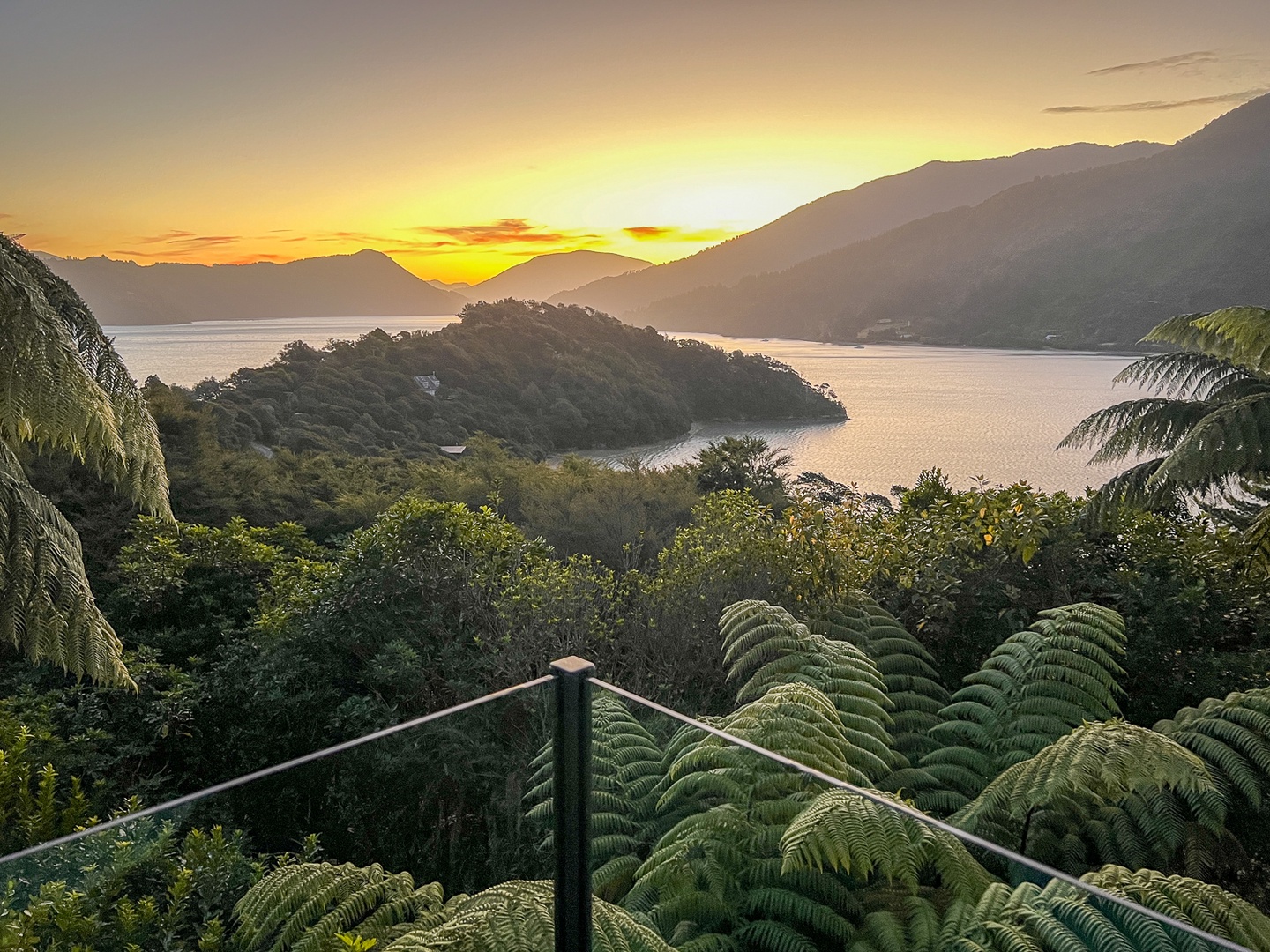 Golden sunset over pristine lake waters surrounded by lush native forest and rolling mountains in this spectacular natural setting.