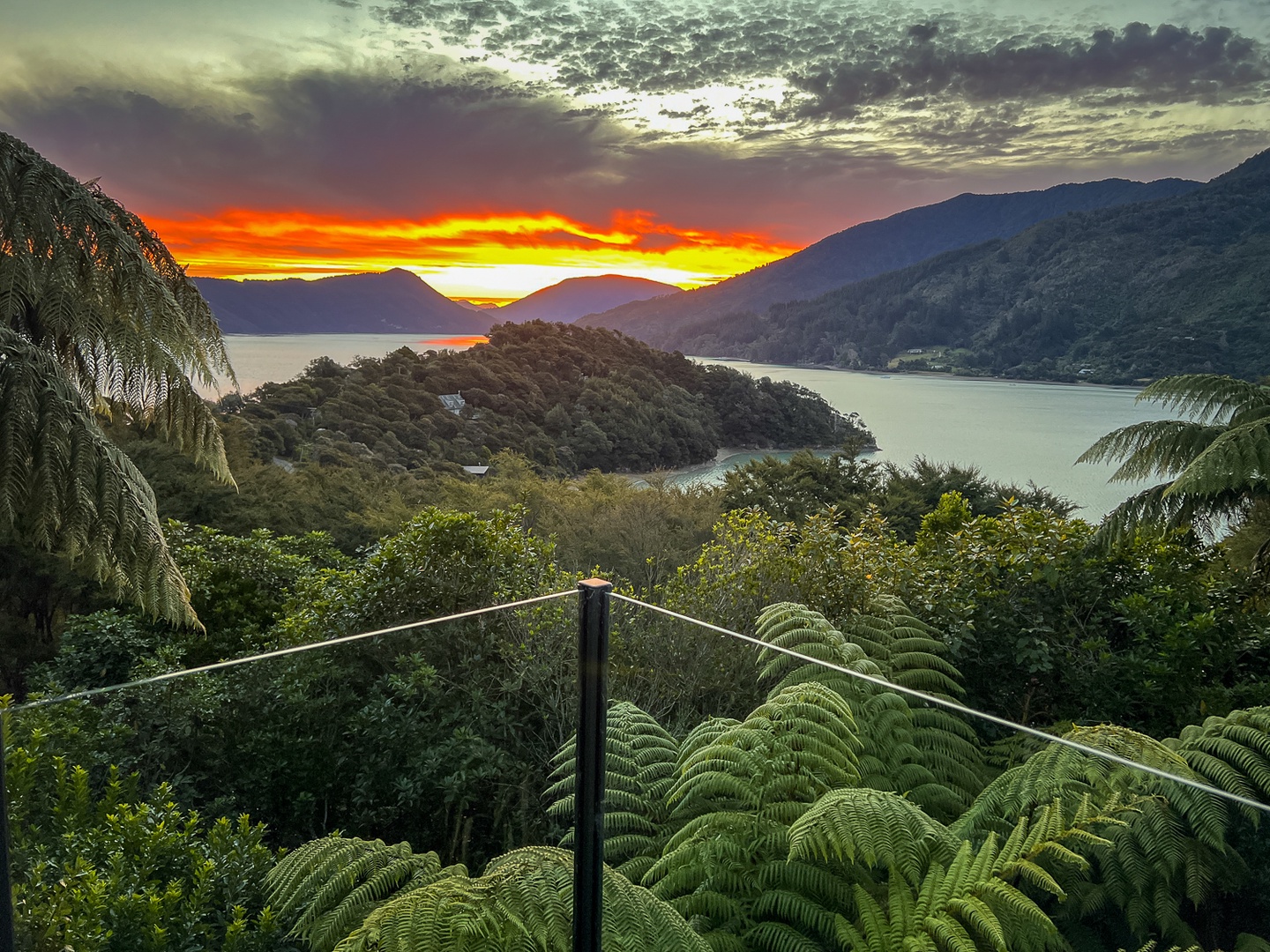 Spectacular sunset paints the sky in brilliant oranges and golds over pristine waters and forested mountains in this stunning natural setting.