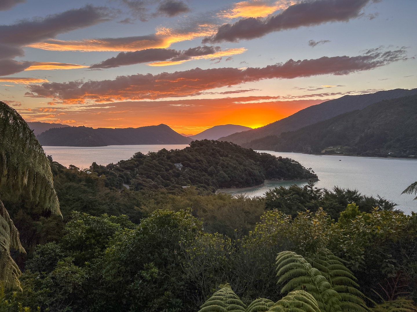 Stunning sunset paints the sky over pristine waters and forested hills in this breathtaking natural setting.