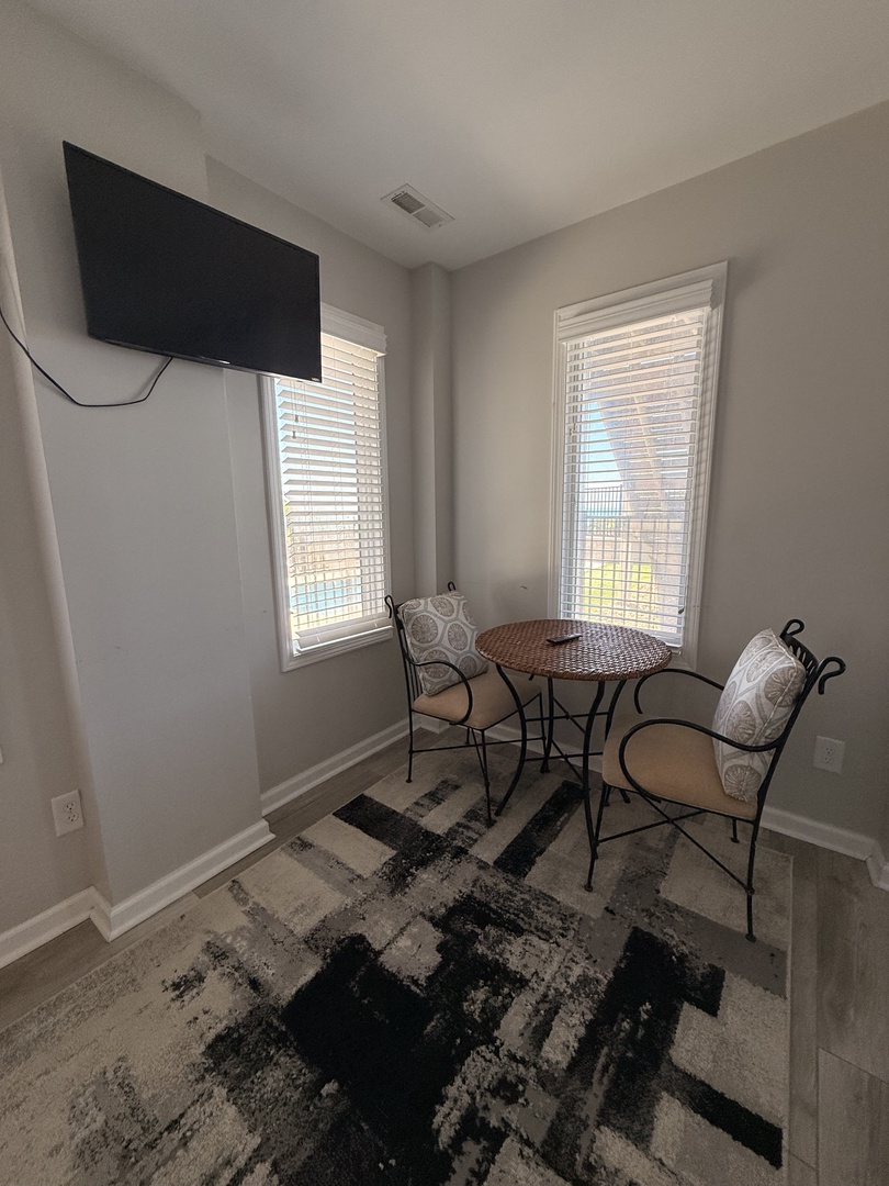 Step into your bright, modern bedroom with natural light streaming through dual windows. A cozy stylized rug adds character, while the sleek TV and chic seating nook invite you to unwind in comfort.