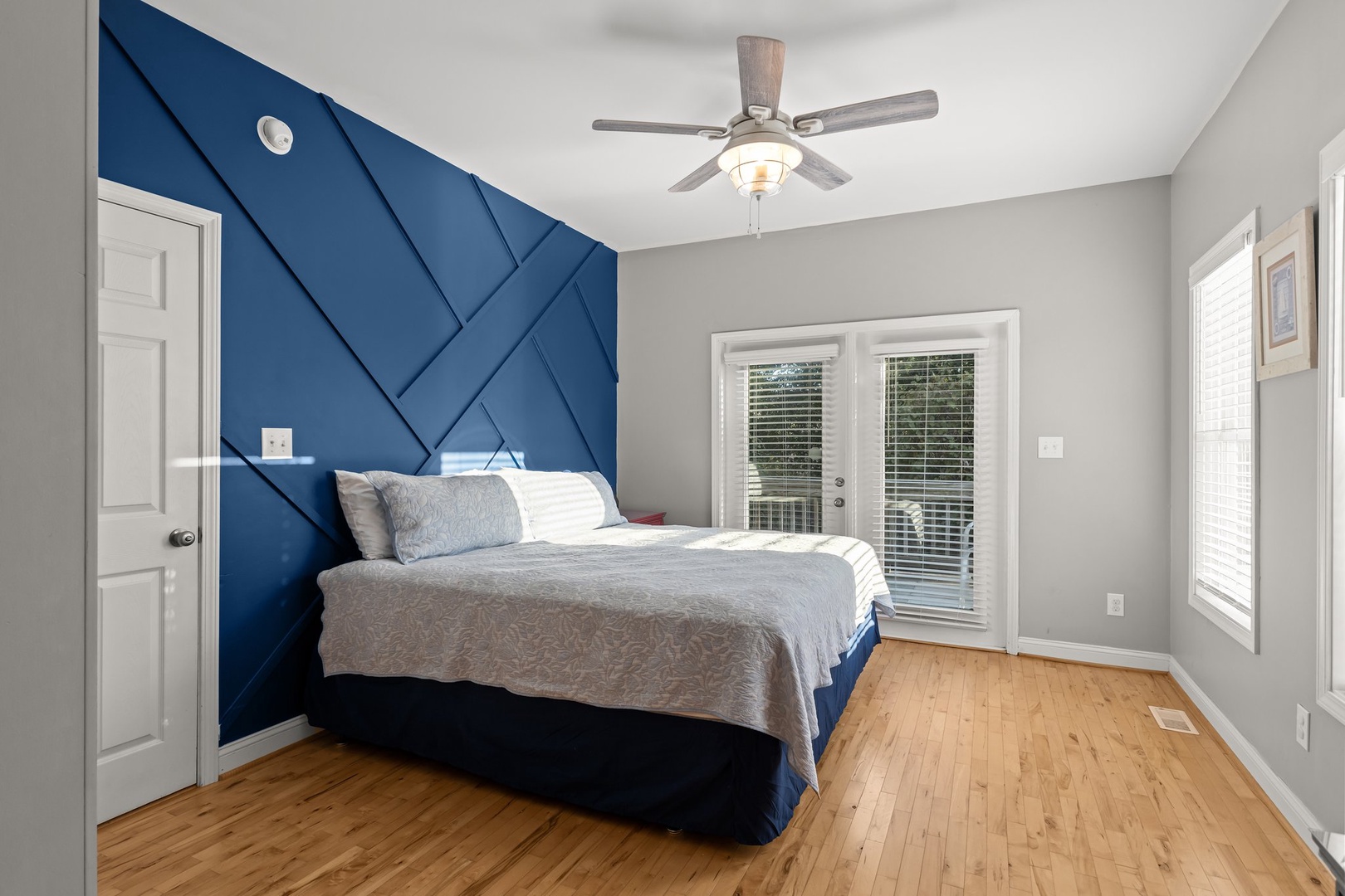 Rest in this stylish bedroom featuring a striking blue accent wall and private balcony access for fresh air and peaceful moments.