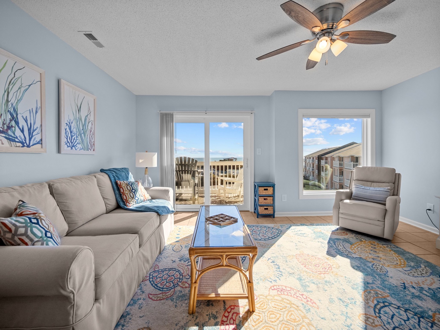 Relax in this bright coastal living space with soft gray furnishings, cheerful blue accents, and balcony access for seaside breezes.