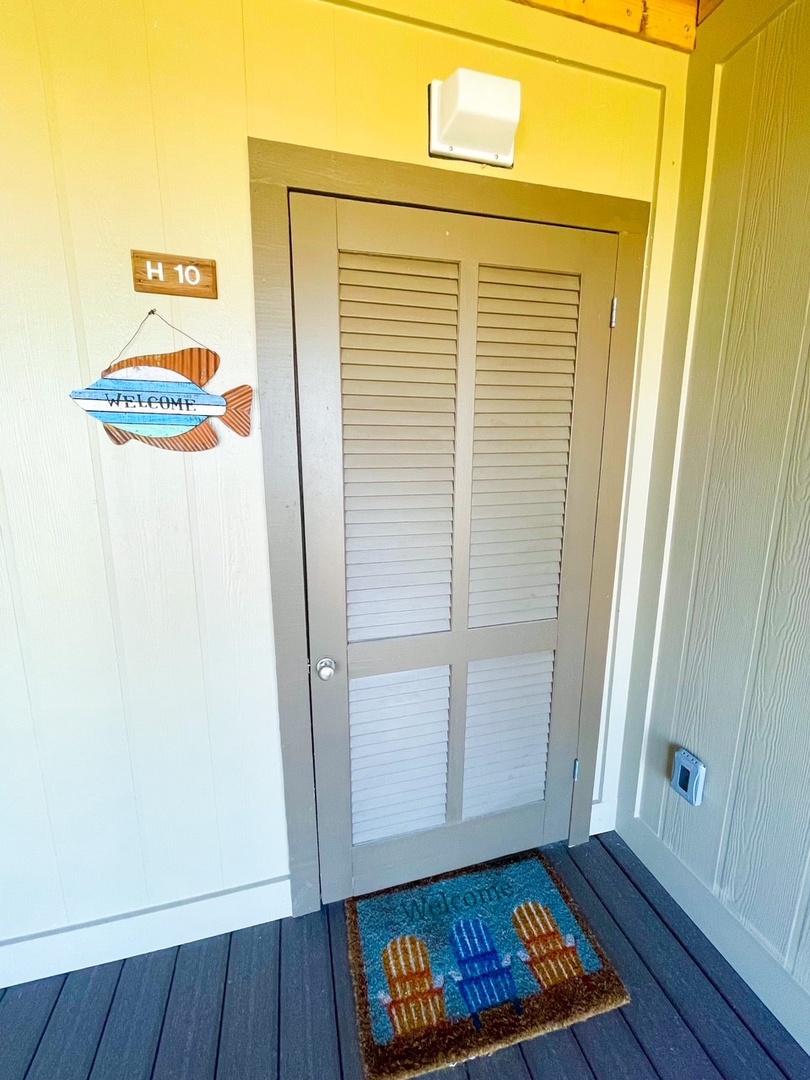 Your coastal retreat awaits behind charming louvered doors, complete with a cheerful beach-themed welcome mat and nautical fish sign.