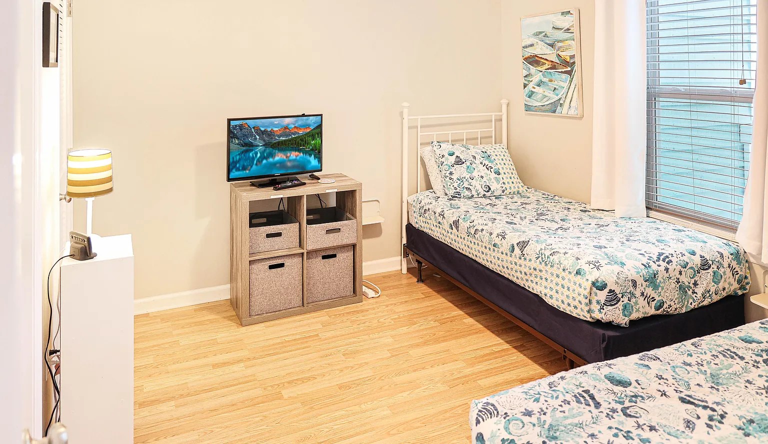 Your bright bedroom features two comfortable beds with coastal-inspired linens, natural wood floors, and a flat-screen TV for relaxing evenings.