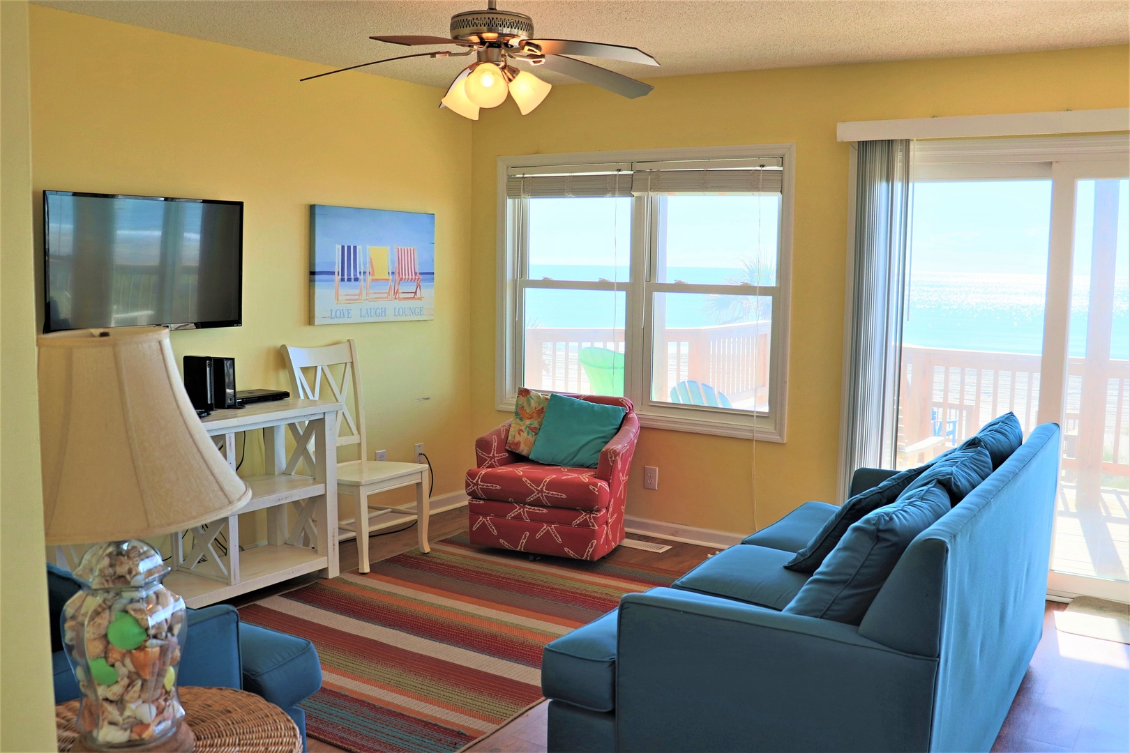 Your bright living space features comfortable seating, ceiling fan, and stunning water views through expansive windows.