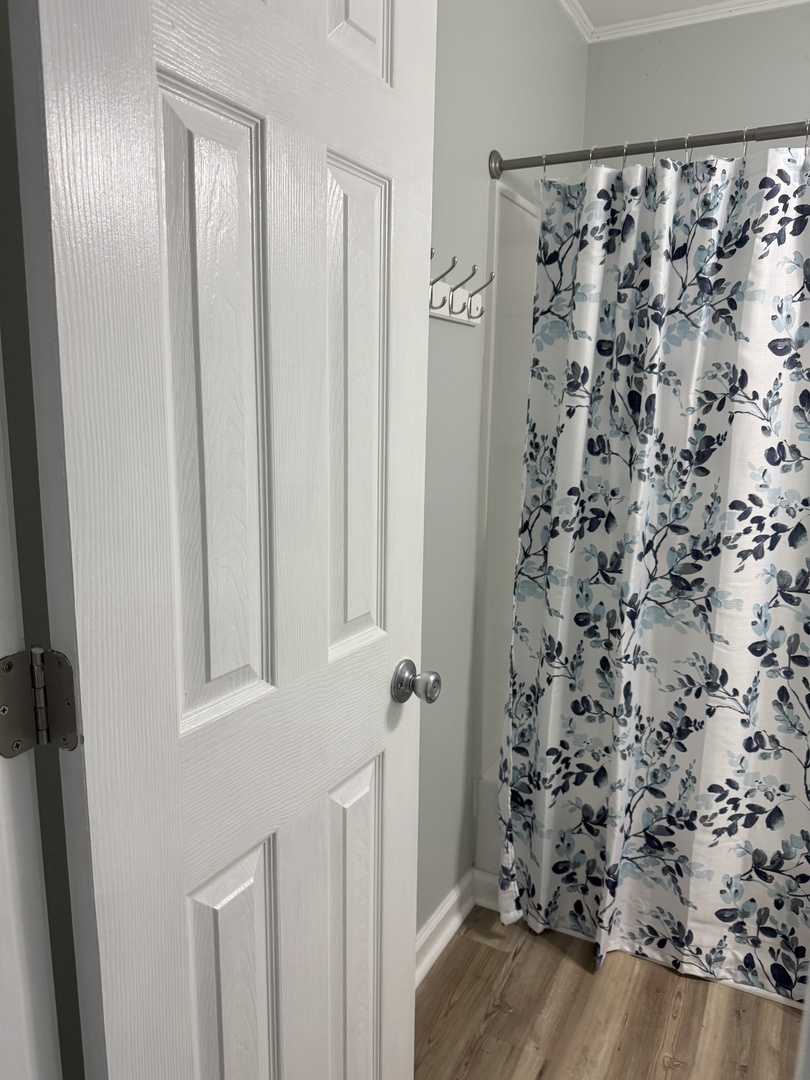 Step into your private bathroom featuring a lovely floral shower curtain and convenient wall hooks for your belongings.