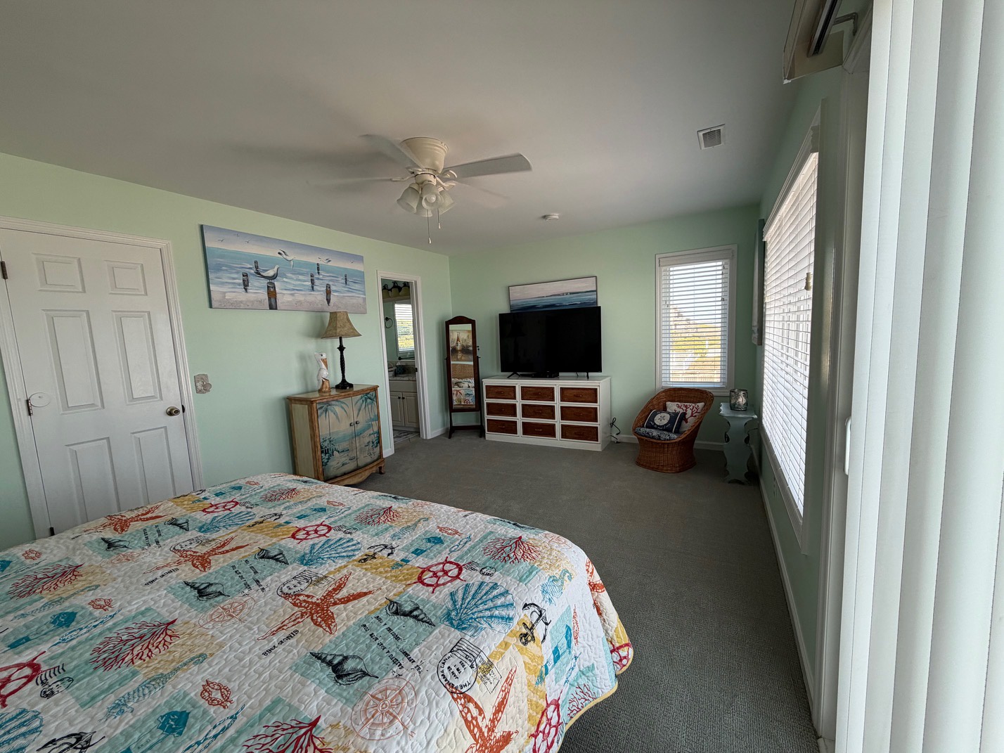 Relax in your spacious coastal-themed bedroom with ocean artwork, cozy seating, and entertainment center for perfect beach vacation nights.
